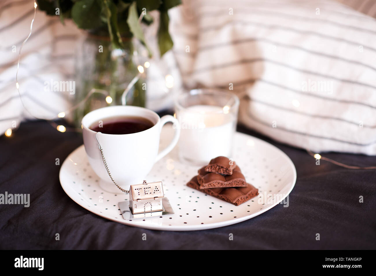 Cup of tea with chocolate bars on plate with candle in bed. Good morning. Stock Photo