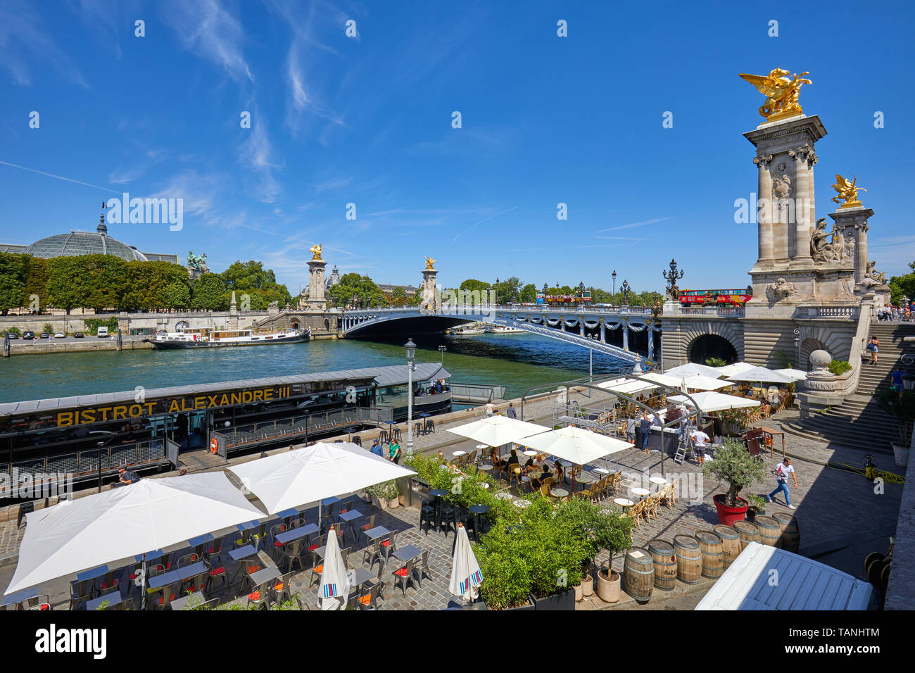 PARIS, FRANCE - JULY 21, 2017: Alexandre III bridge with people and tourists and cafe in docks area in a sunny summer day, blue sky in Paris, France. Stock Photo