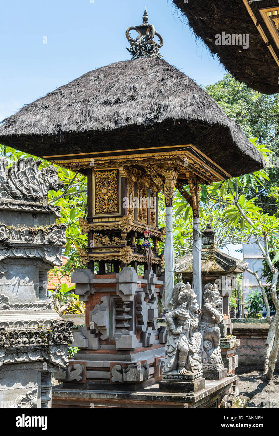 Dusun Ambengan, Bali, Indonesia - February 25, 2019: Decorated gray stone memorial pillar at family compound in garden with green foliage under blue s Stock Photo