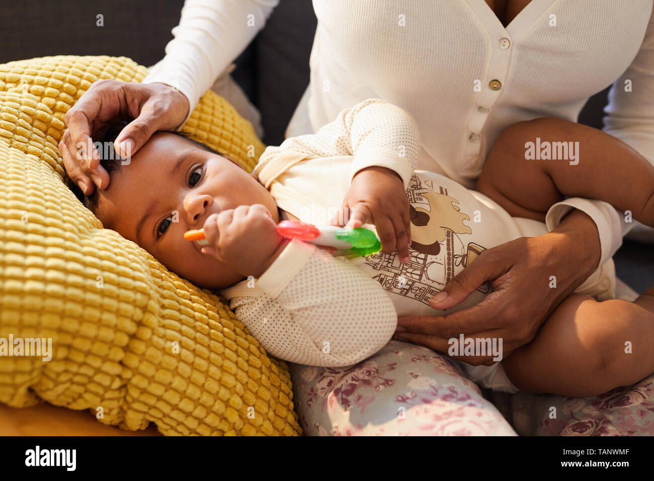 Close-up of curious cute baby boy in bodysuit lying on pillow and biting rubber toy while having teething Stock Photo