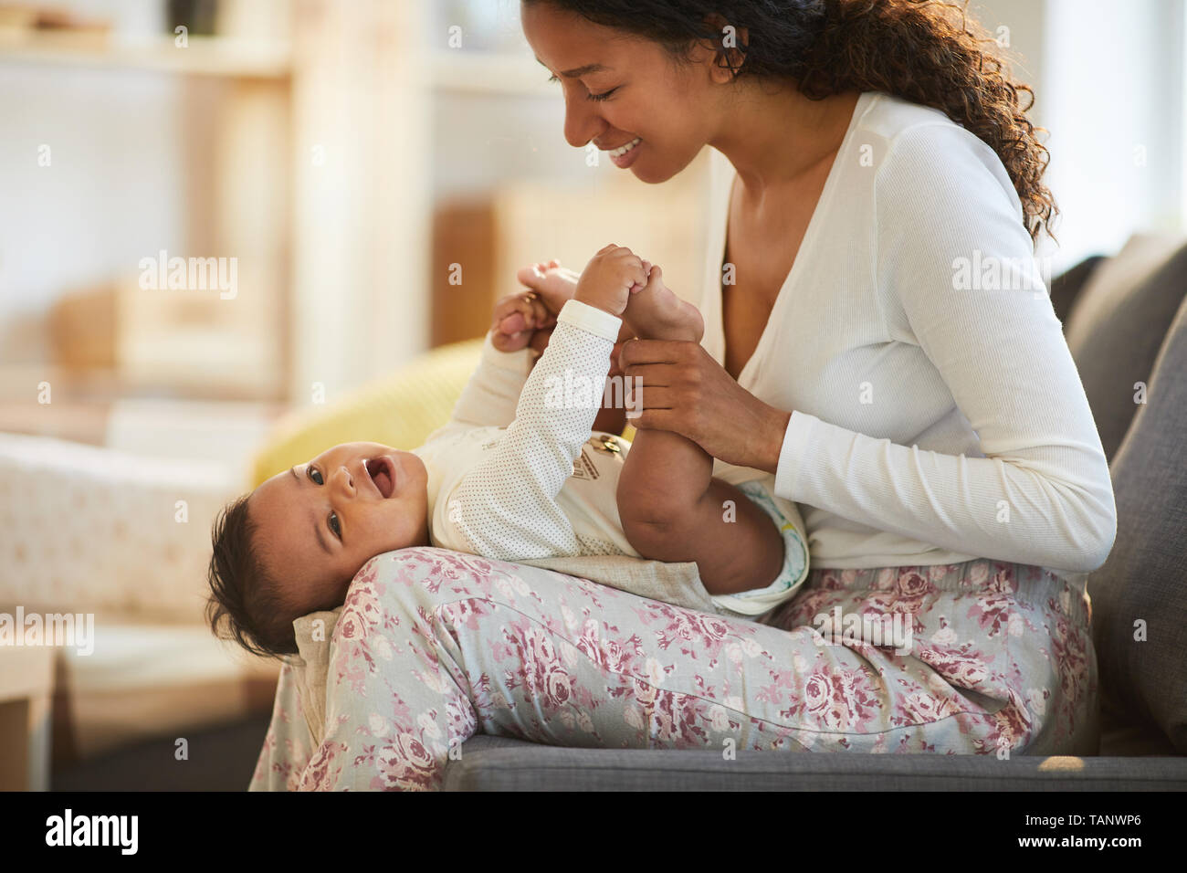 Happy excited young black mother in homewear sitting on sofa and touching  little legs of baby while having fun with infant son Stock Photo - Alamy