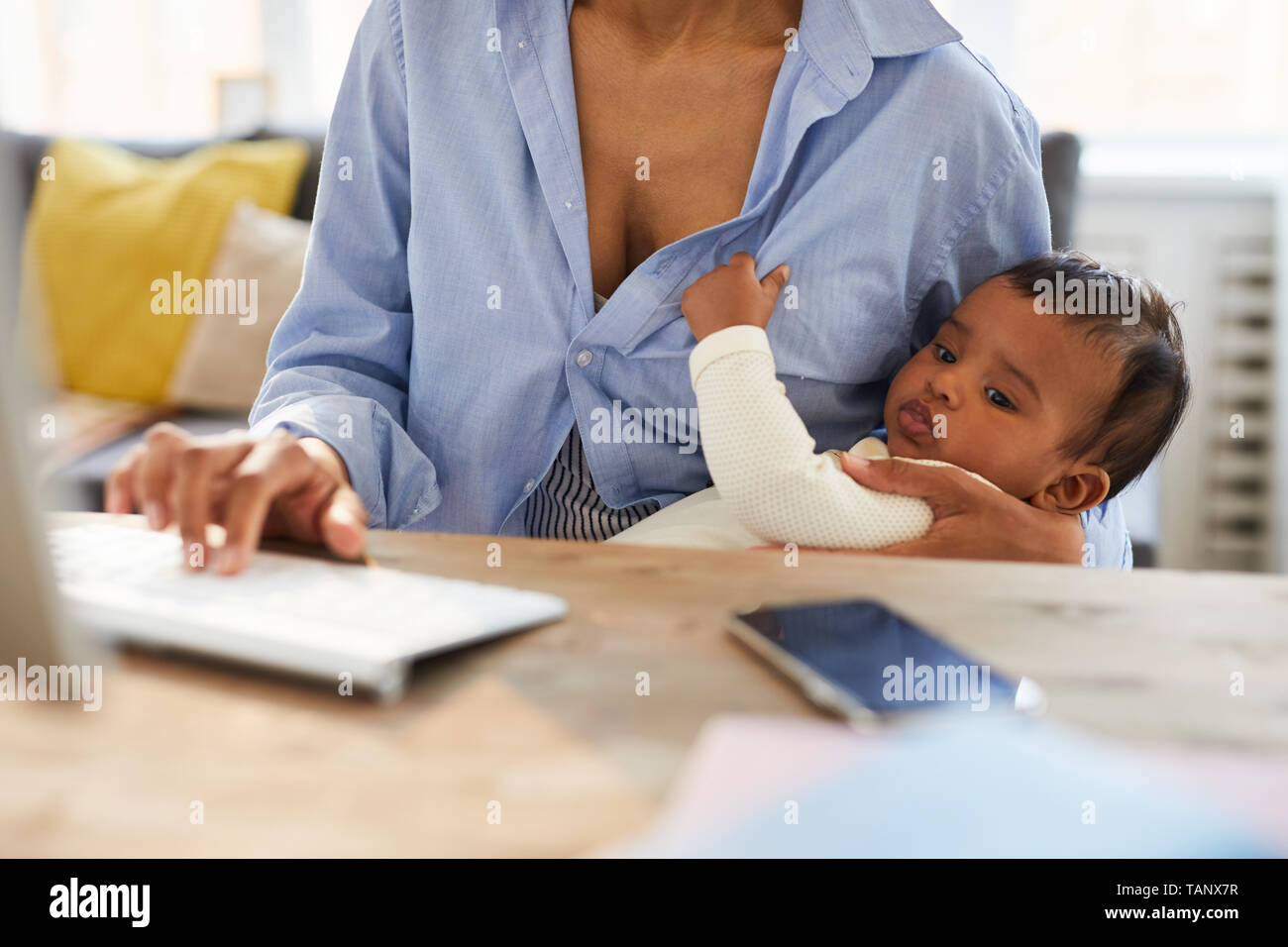 Close-up of concentrated African baby boy keeping mothers shirt and looking at computer monitor while his mother working on project Stock Photo