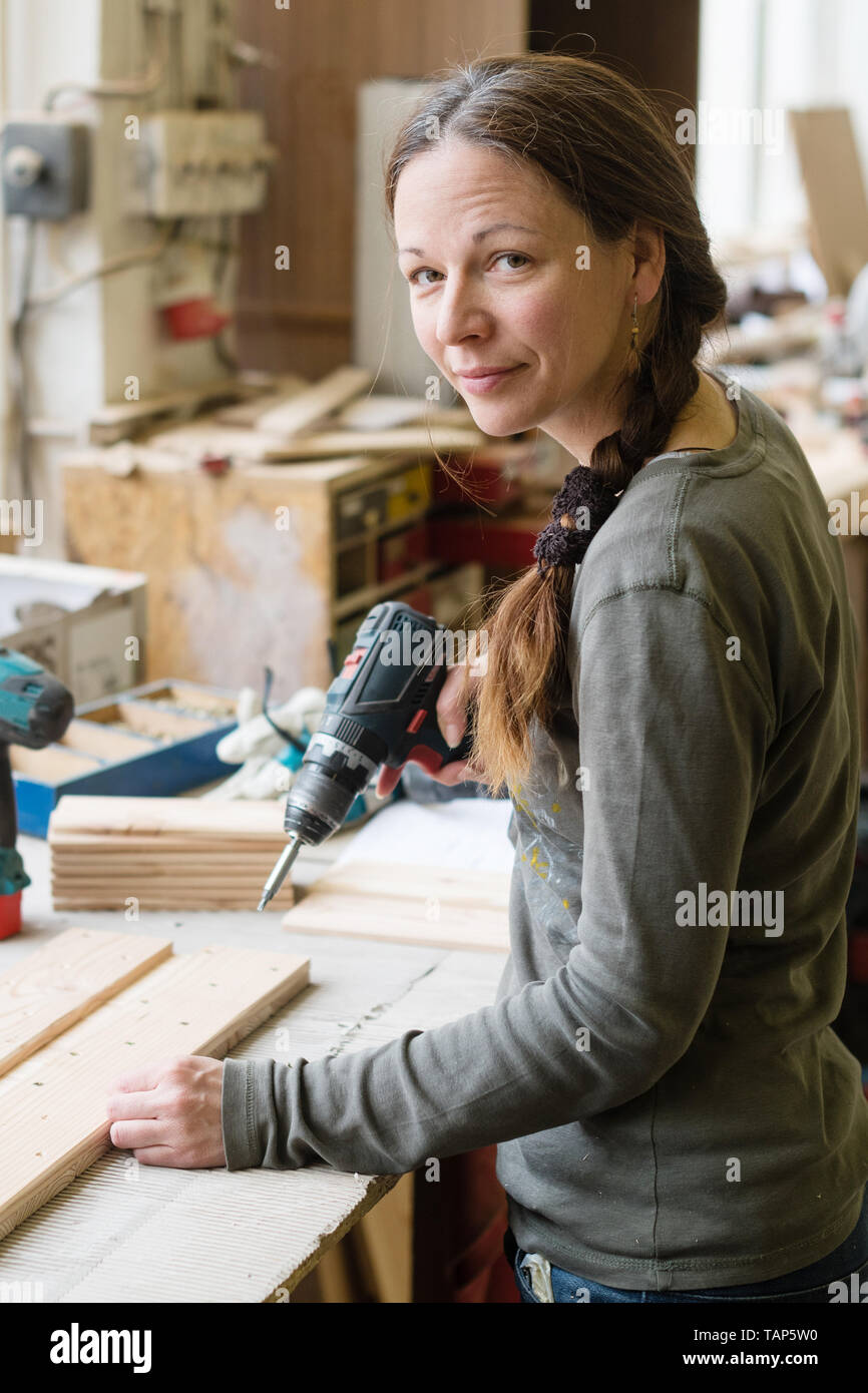 Young woman using a electric screwdriver on a piece of wood at workshop Stock Photo