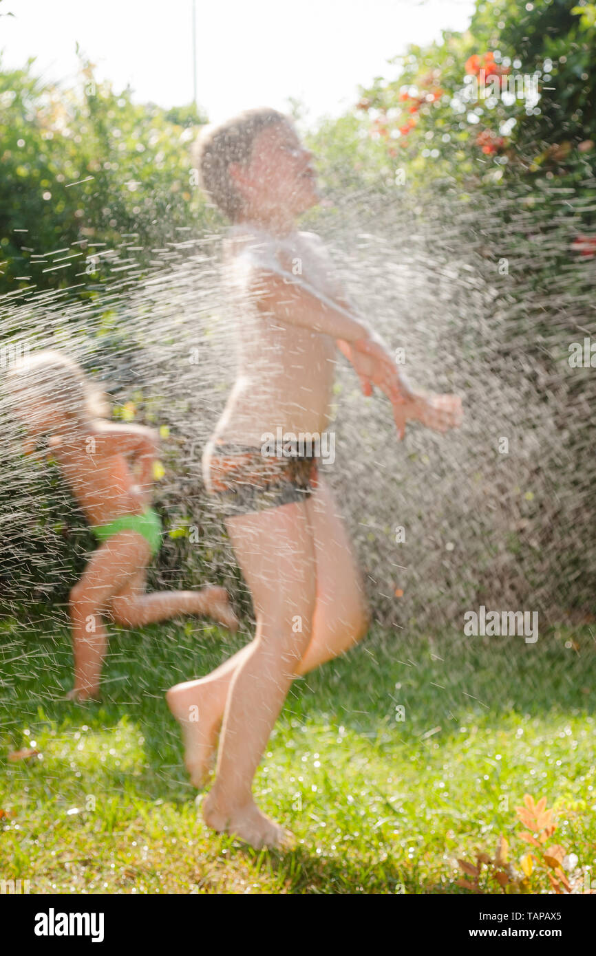 Happy children having fun palying with lawn sprinkler in a summer garden - summer holidays concept Stock Photo