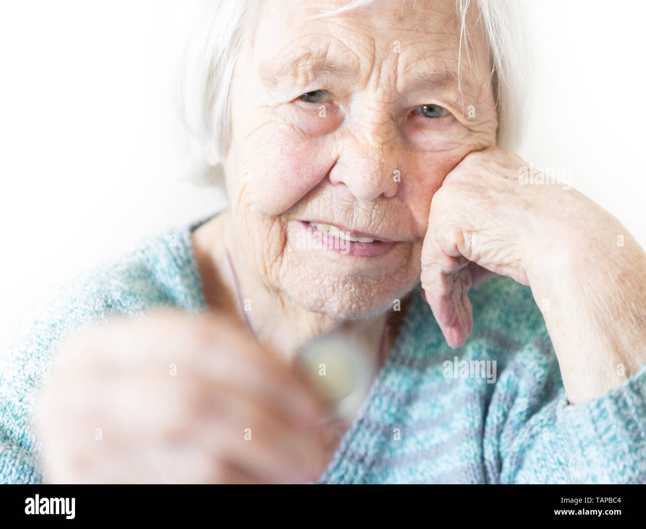 Cheerful elderly 96 years old woman sitting at table at home happy with a coin in her hand. Saving for retirement and financial planing concept Stock Photo