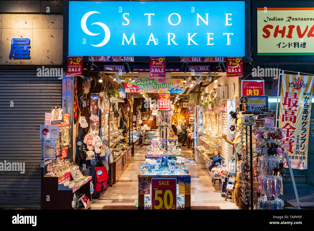 Kumamoto City, Japan. 'Stone Market' teenage fashion accessory shop in shopping arcade. Looking into open shop, illuminated at night, 2 people inside. Stock Photo