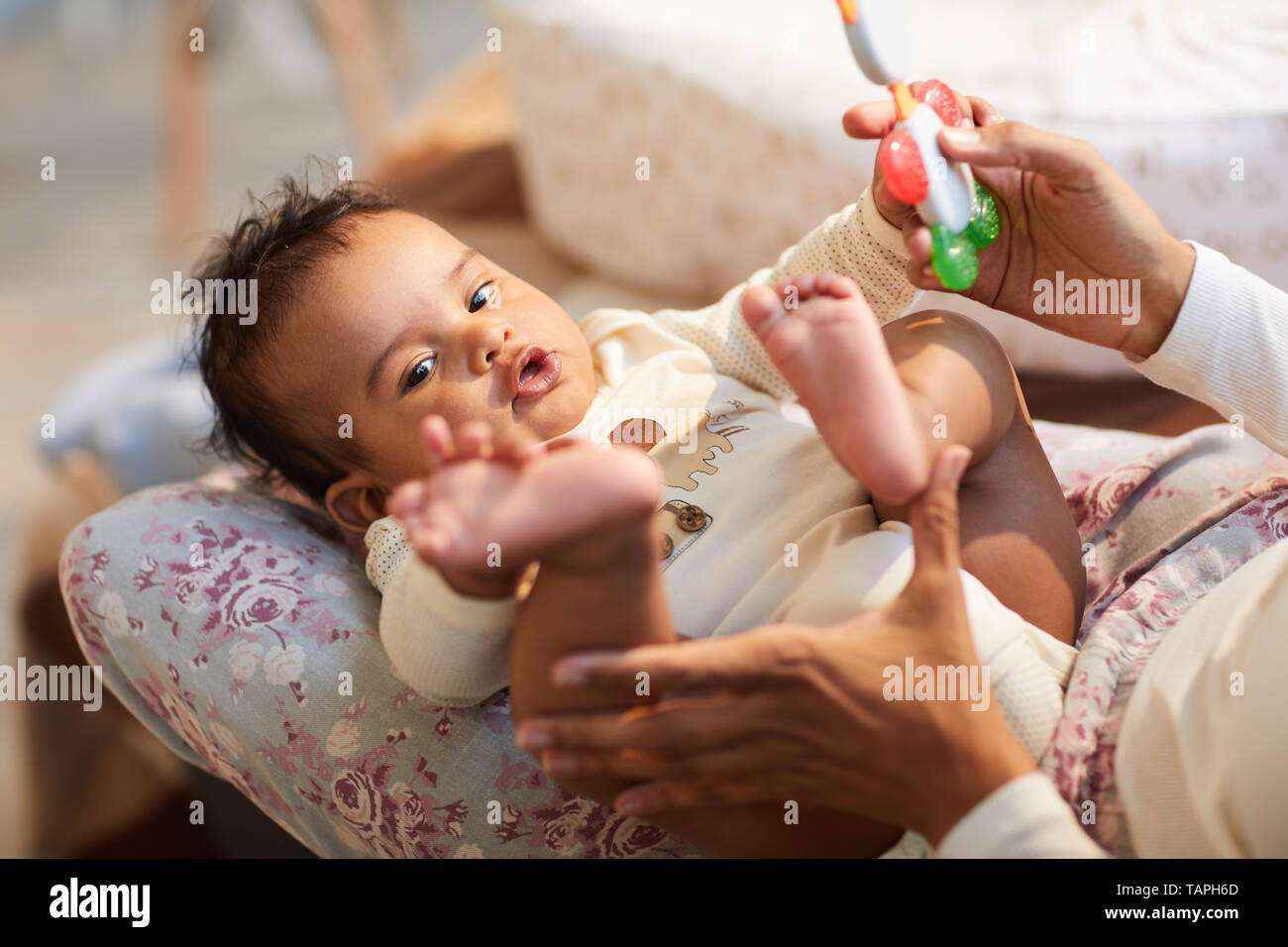 Close-up of curious cute baby with ratty hair lying on mothers knees and touching own foot, mother playing with baby Stock Photo