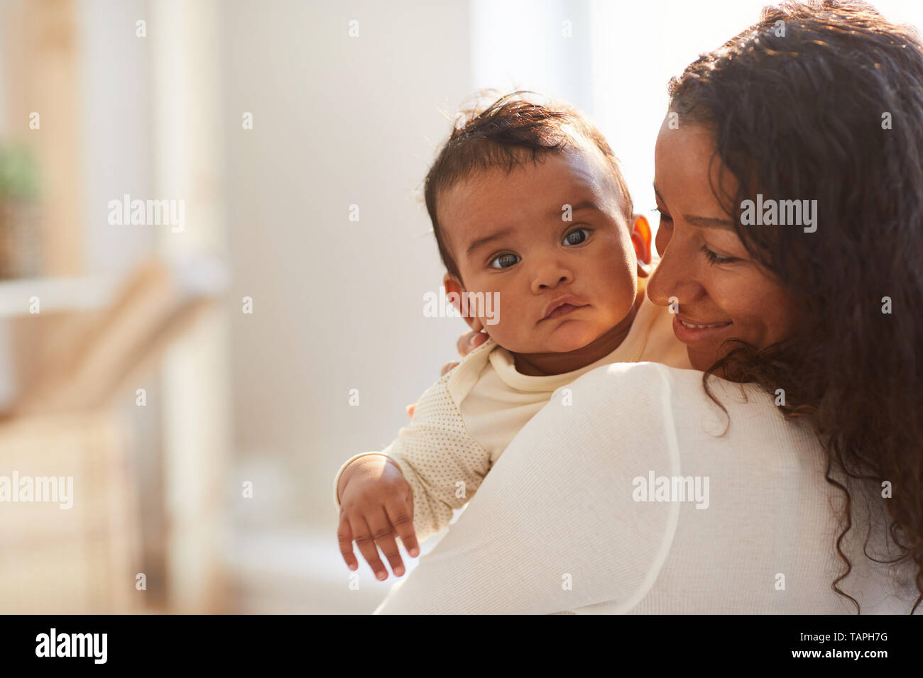 Smiling loving young African mom with curly hair standing in room and holding adorable baby boy with chubby cheeks Stock Photo