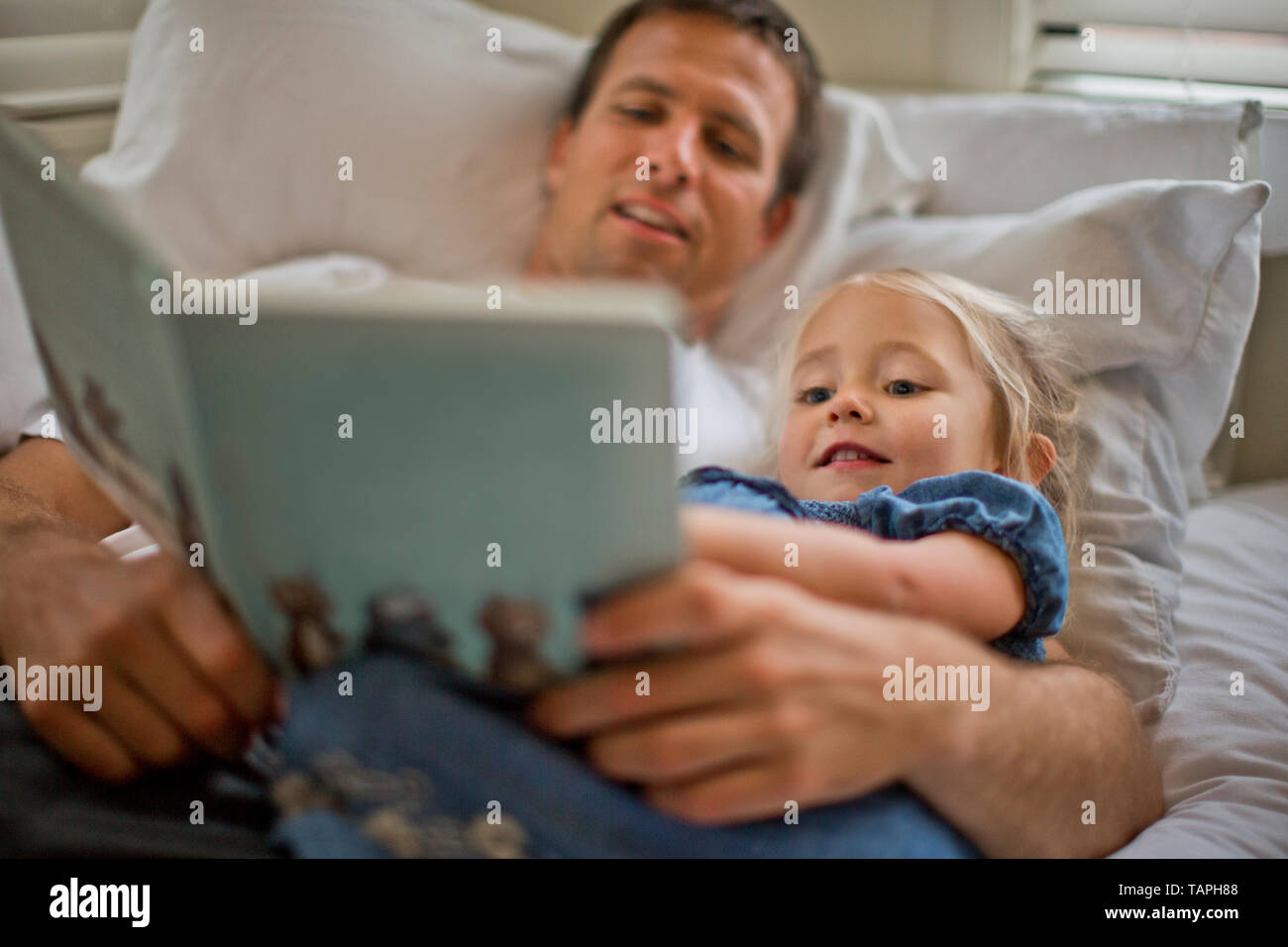 Father lying down reading a book with his daughter. Stock Photo