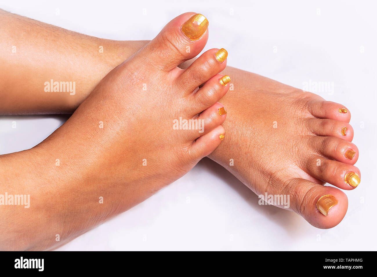 Female feet with carefully pedicured fashionable golden nails displayed in the crossed position on Isolated white Background Natural look. Stock Photo