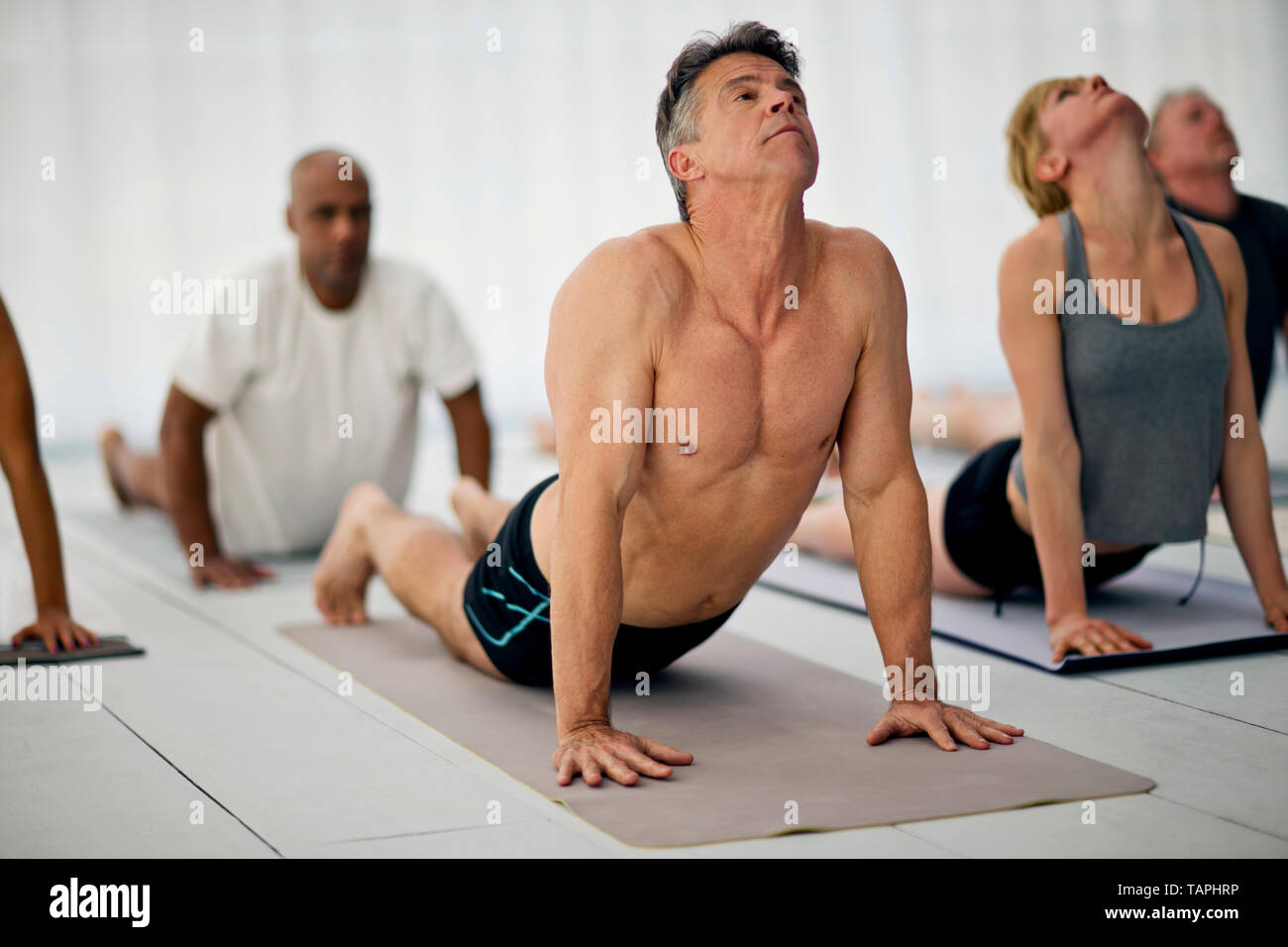 Group of yoga class attendees stretch upward halfway through a salute to the sun routine. Stock Photo