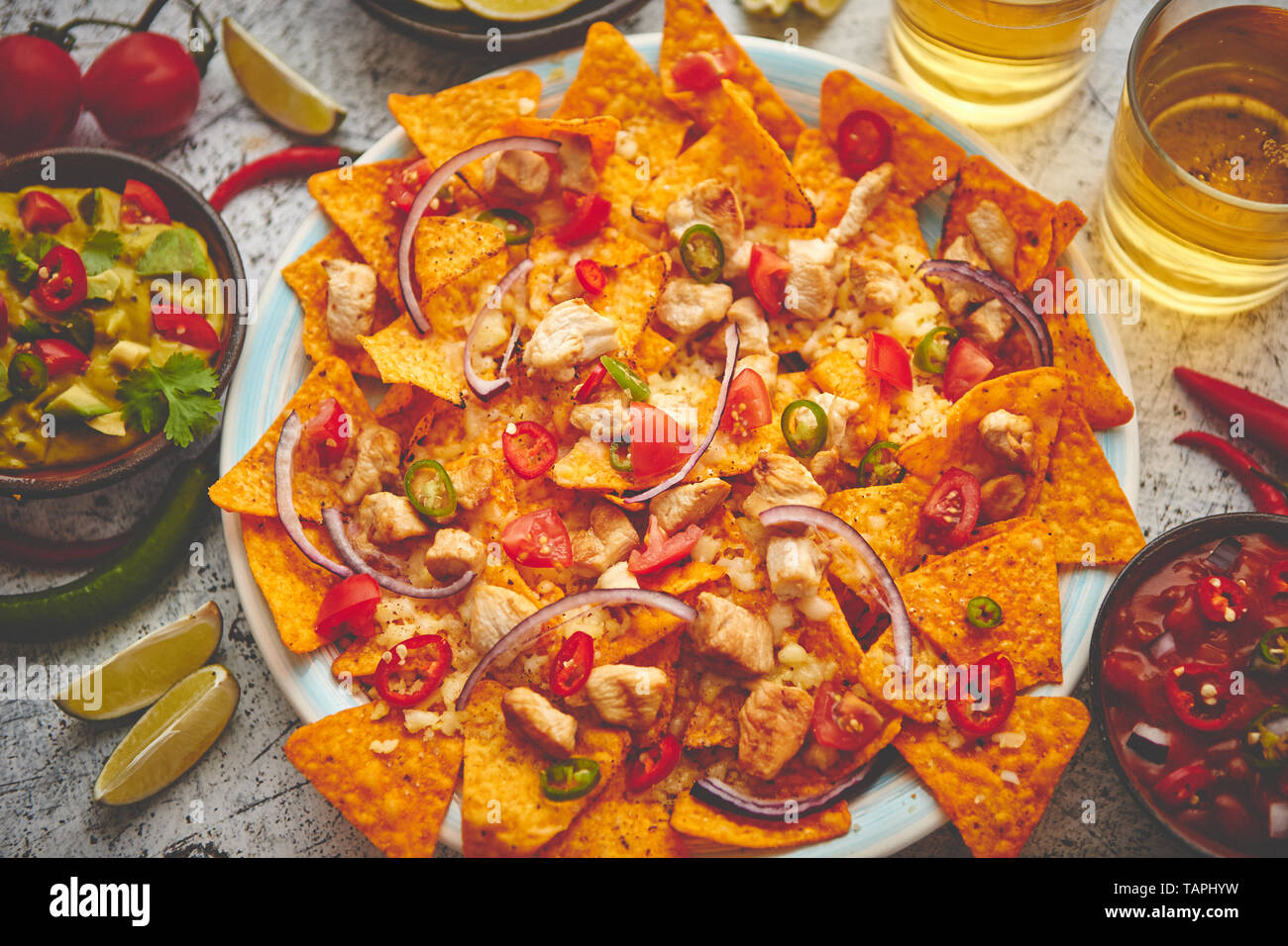 Mexican corn nacho spicy chips served with melted cheese, peppers, tomatoes, beer and side salsas. Stock Photo