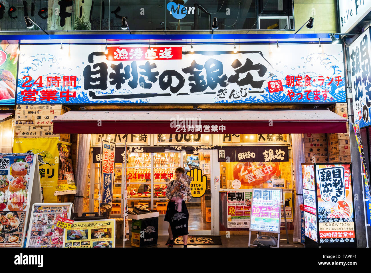 Kumamoto City. Night scene, Shimotori shopping arcade. Front exterior and entrance of Mekiki no Ginzi seafood restaurant with promo woman holding menu Stock Photo