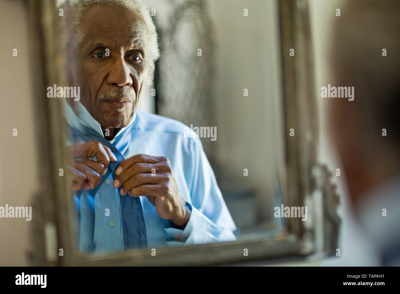Senior man fixing his tie in the mirror. Stock Photo