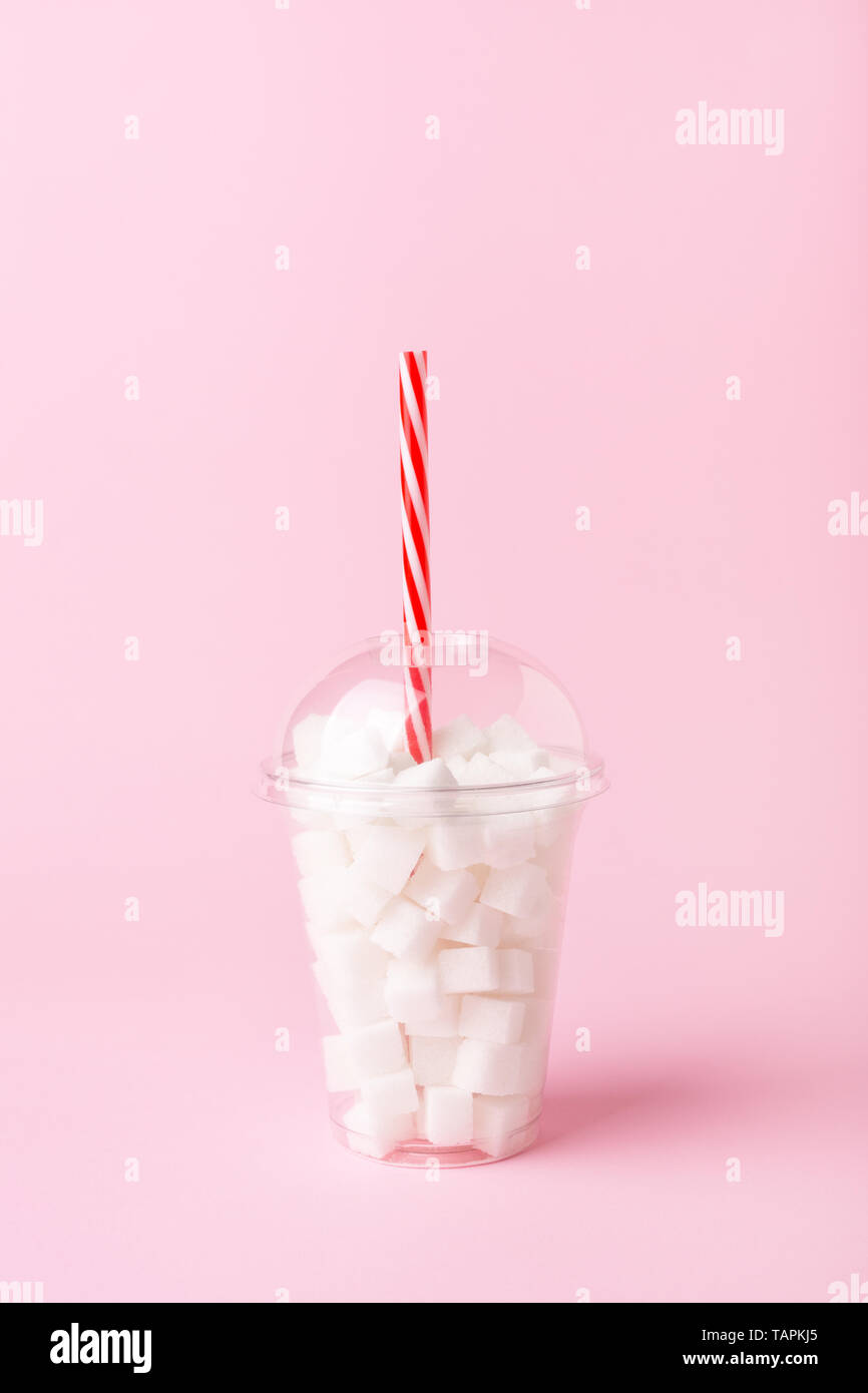 Plastic shake glass with straw full of sugar cubes on pastel pink background. Unhealthy diet concept. Minimal, vertical, side view. Stock Photo