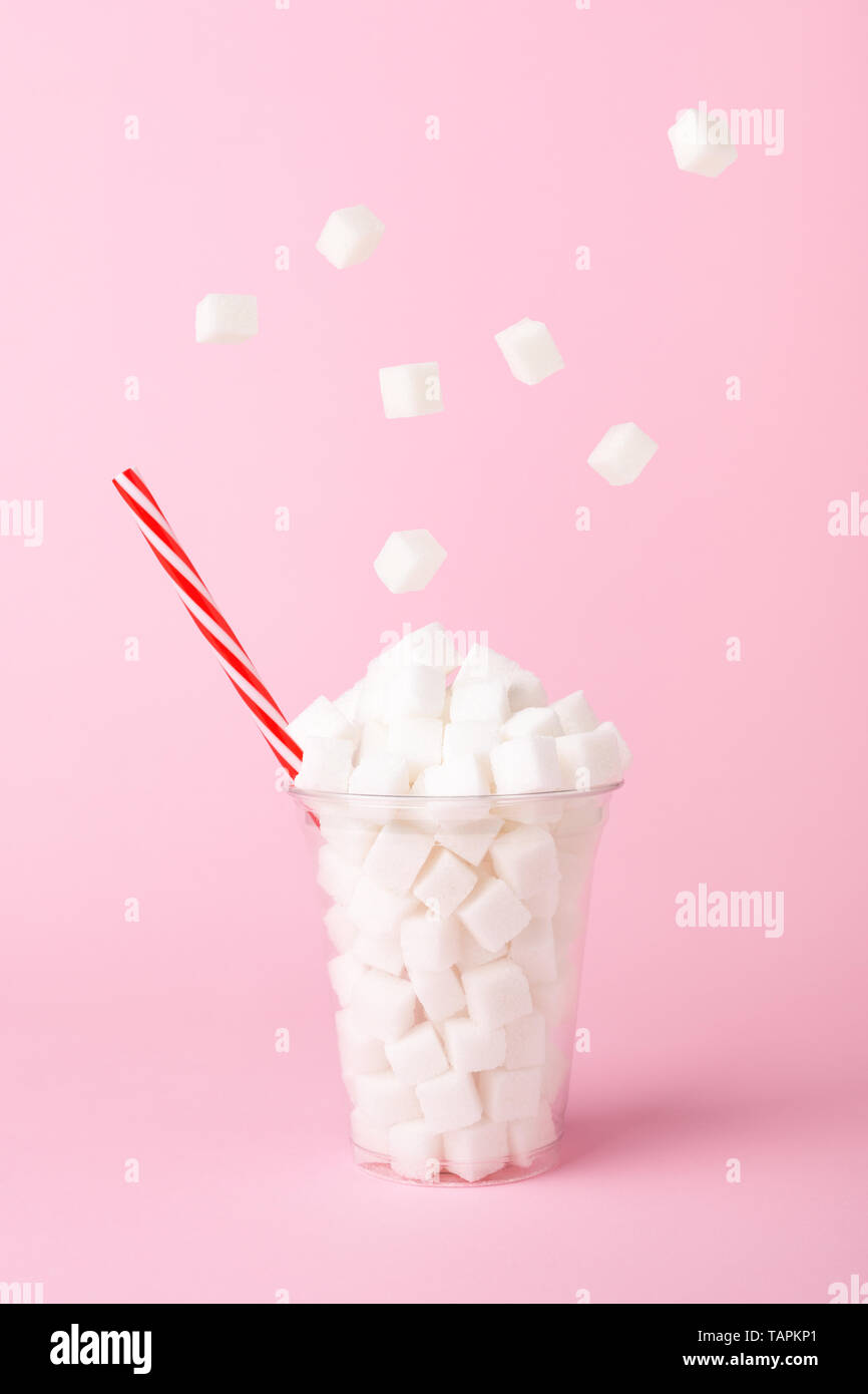 Sugar cubes falling into glass on pastel pink background. Unhealthy diet concept. Minimal, food levitation, side view. Stock Photo