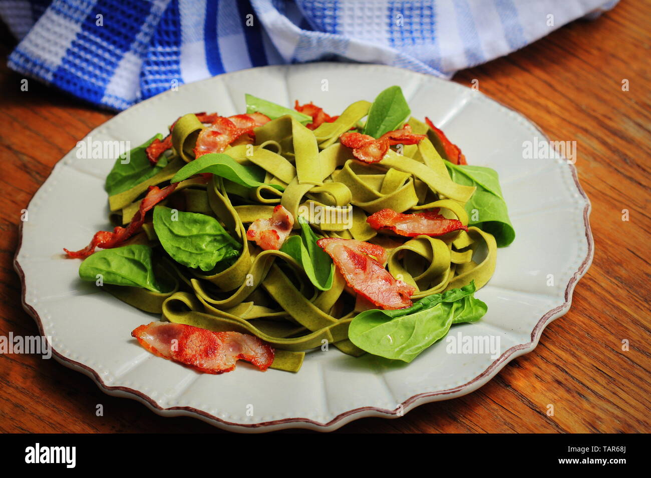 Green spinach pasta with chrispy bacon on wooden table. Gourmet italian