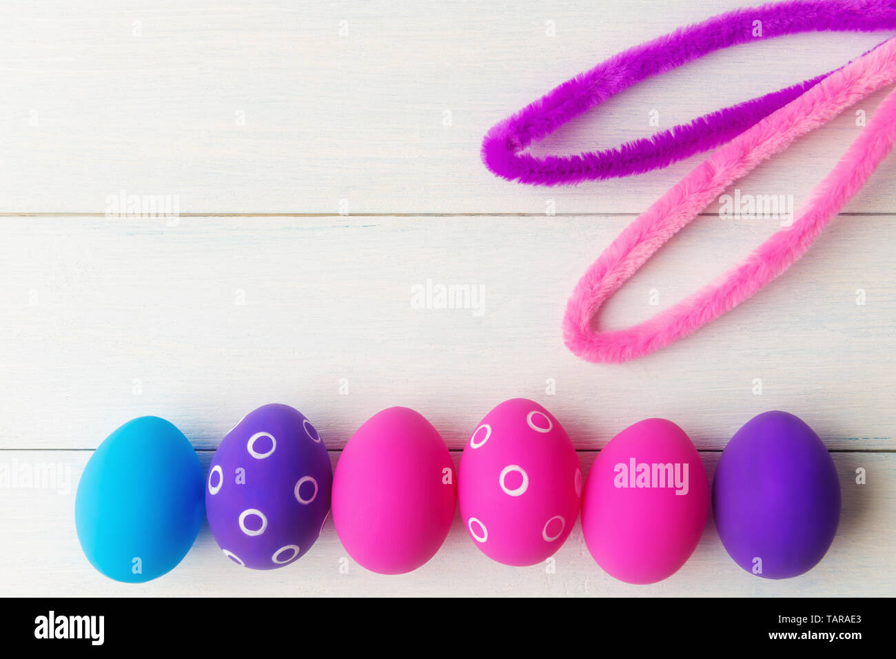 Bunny ears and decorative pink and purple eggs on wooden background with copy space Stock Photo