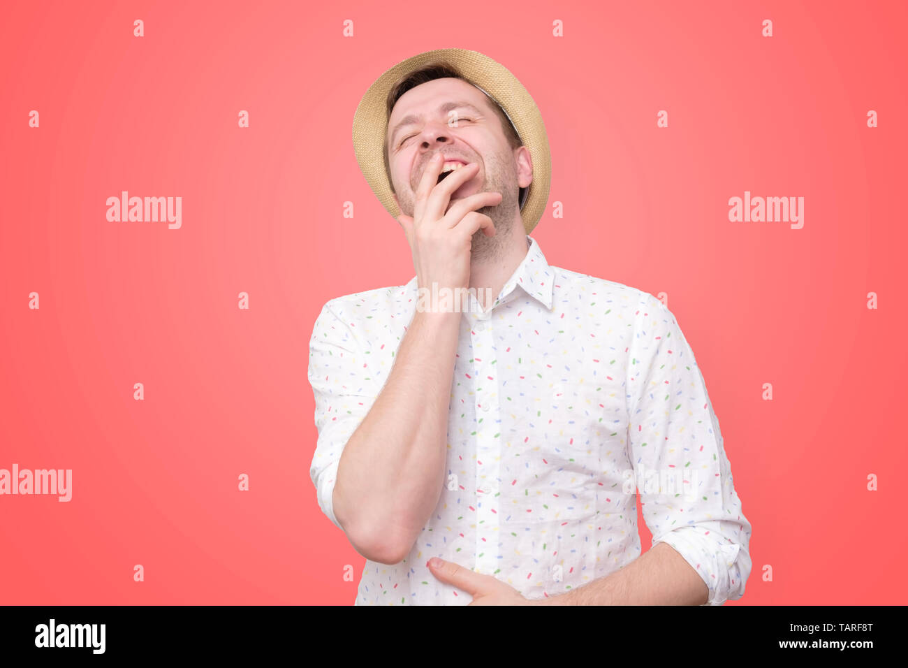 man in summer hat laughs loud on red wall Stock Photo
