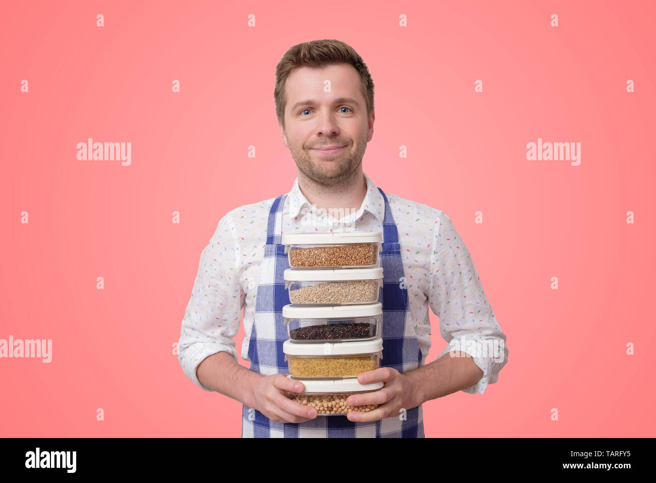 Young smiling man in apron hold several boxes with cereals Stock Photo