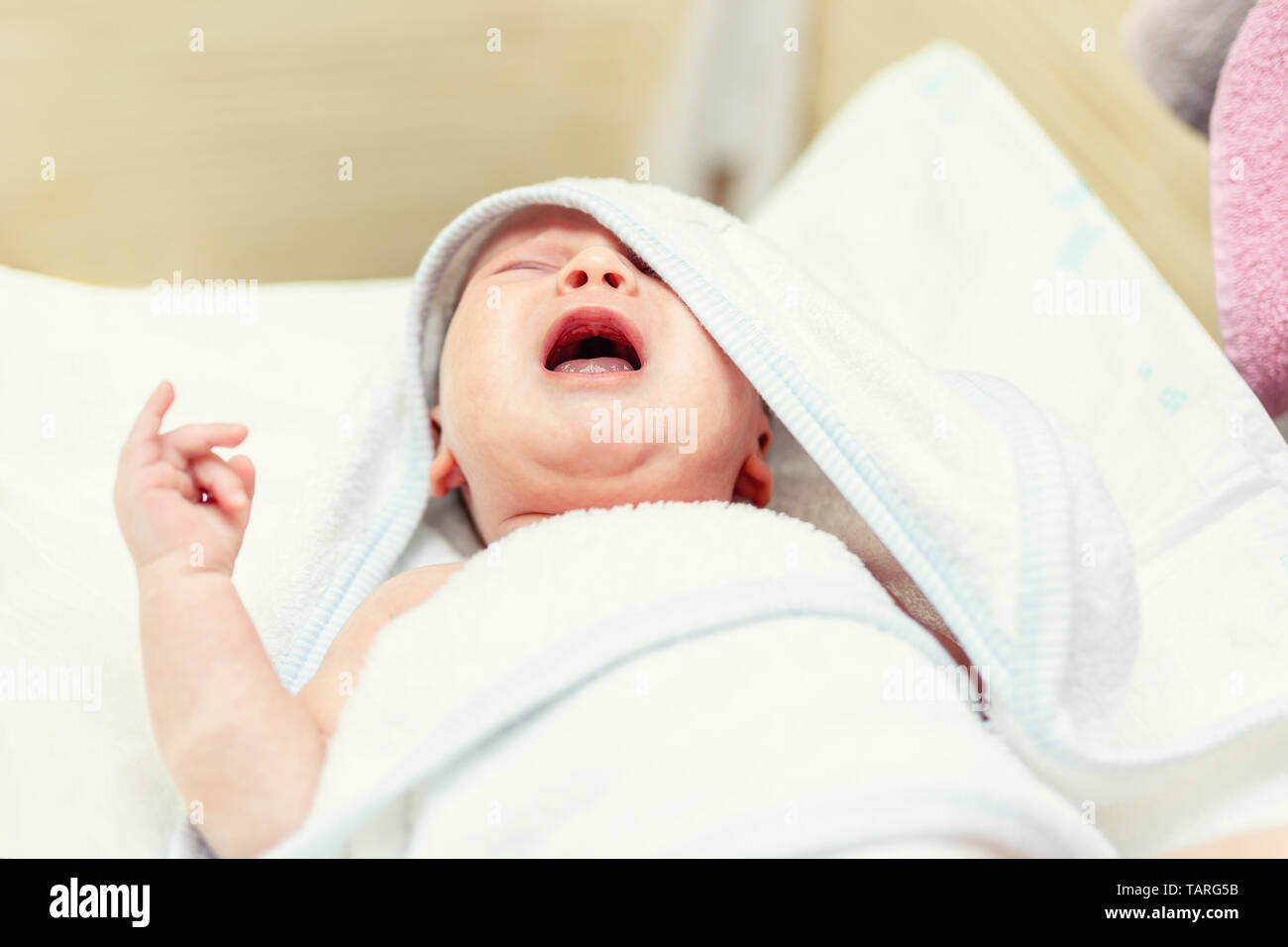 Cute infant baby in white towel crying after first bathing at bathroom. Newborn children healthcare and hygiene Stock Photo