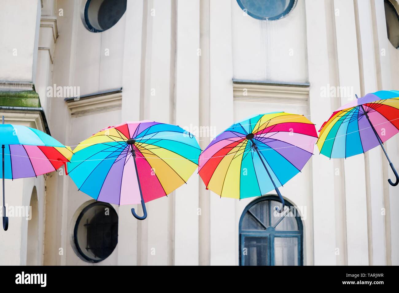 Colored bright rainbow umbrellas on the light old wall background Stock Photo