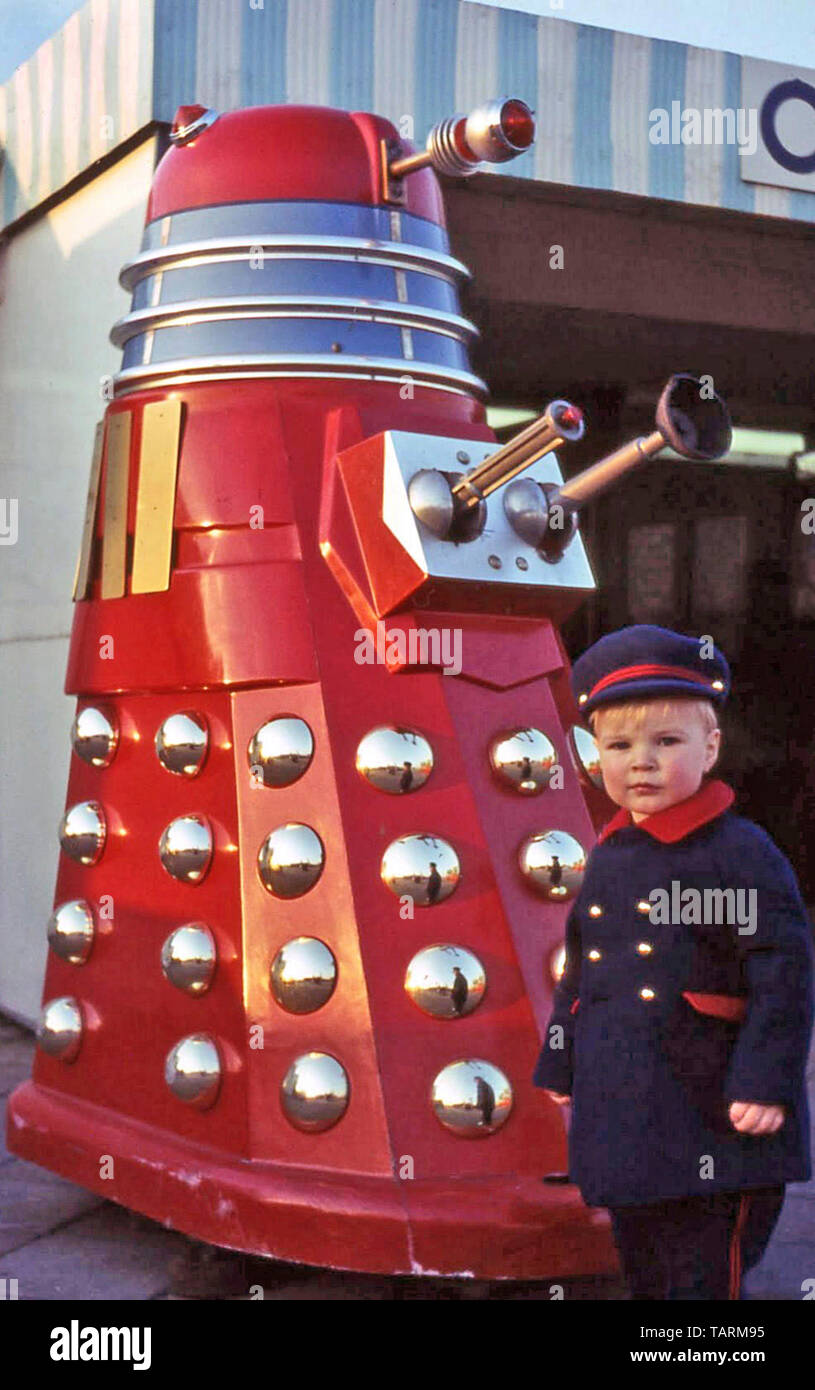 Archival toddler boy in 1960s Sunday best clothing poses beside replica of famous Dalek mutant from BBC science fiction television programme London UK Stock Photo