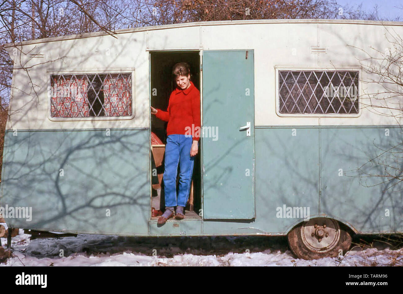 Archival 1960s just married young woman standing in doorway of dilapidated old caravan snow covered building site first marital home 60s England UK Stock Photo