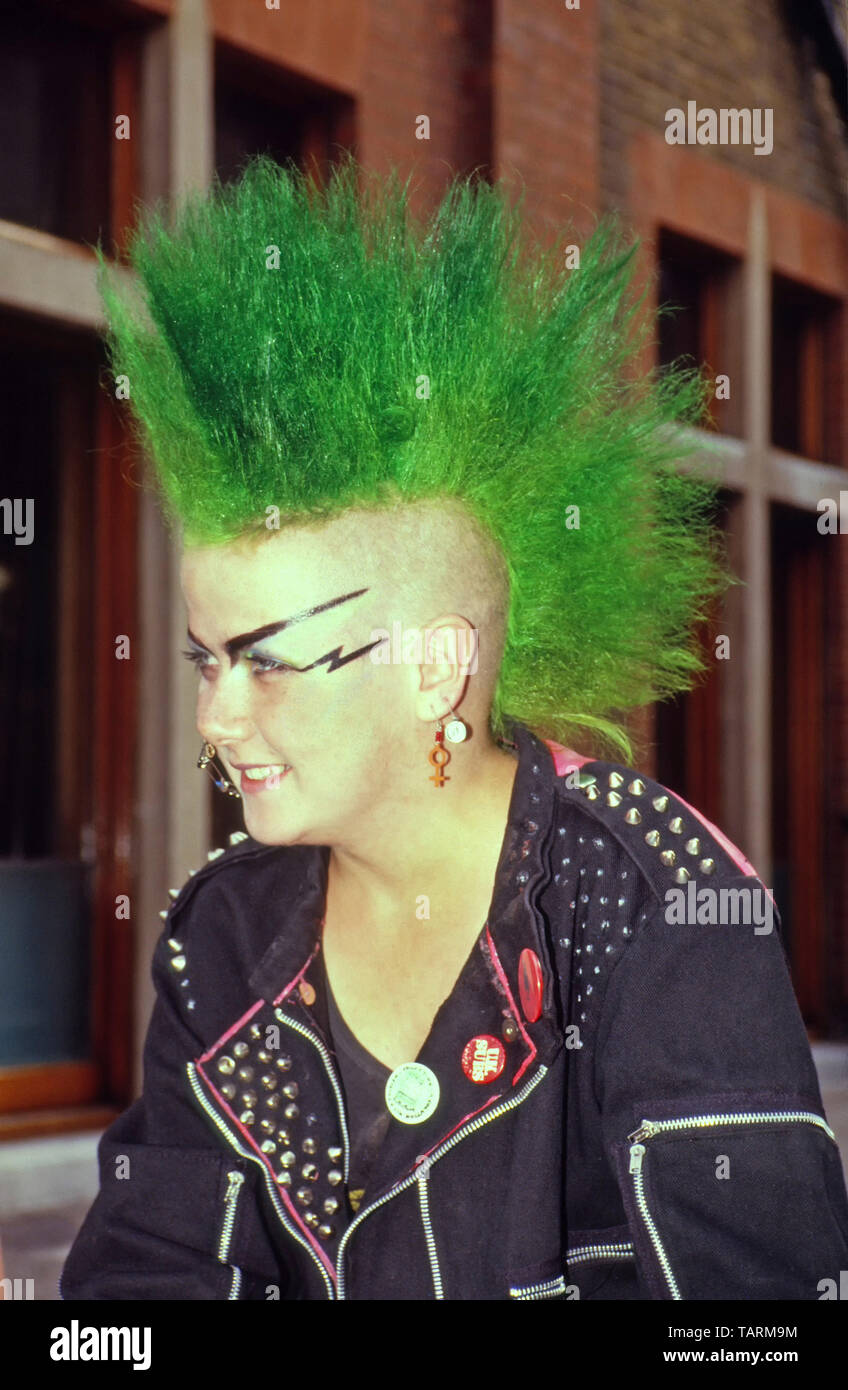 Punk 1980s teenage girl green spikey mohican hair style & face paint pose for photo & hanging out in public area Covent Garden London England UK Stock Photo