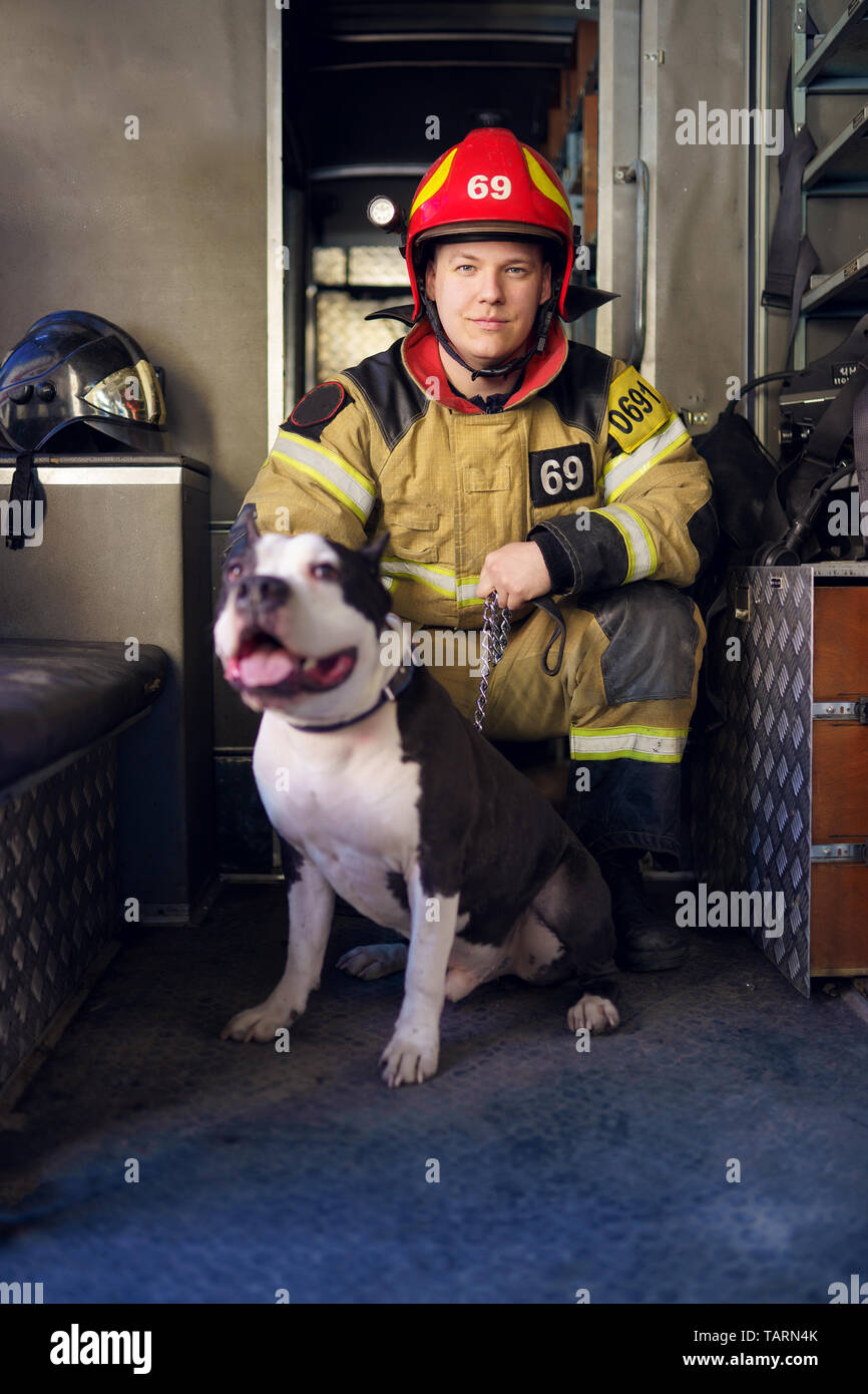 Image of man fireman with lifeguard dog on background of fire