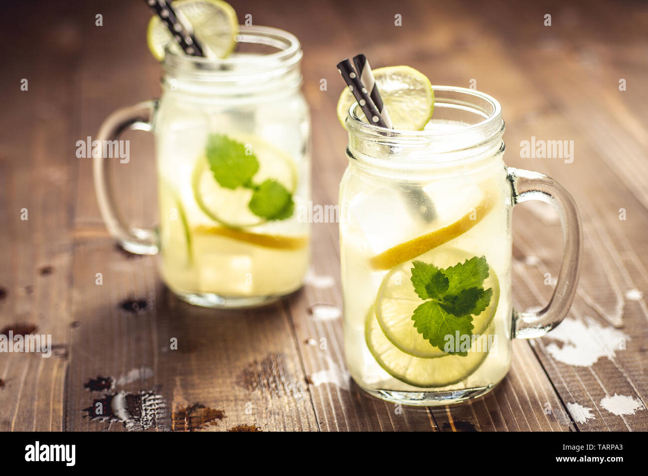 Cold Fresh Mojito Cocktail Lemonade with Ice, Lemon and Mint Leaves in Mason Jar on Rustic Dark Wooden Background. Summer Concept. Stock Photo