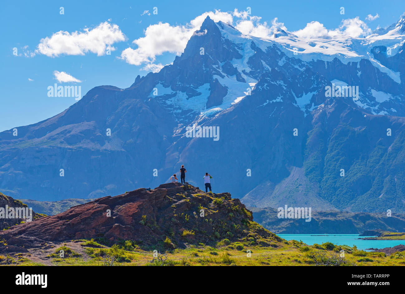 Three tourists looking upon Lake Pehoe and the Andes peaks of Torres and Cuernos del Paine, Torres del Paine national park, Patagonia, Chile. Stock Photo