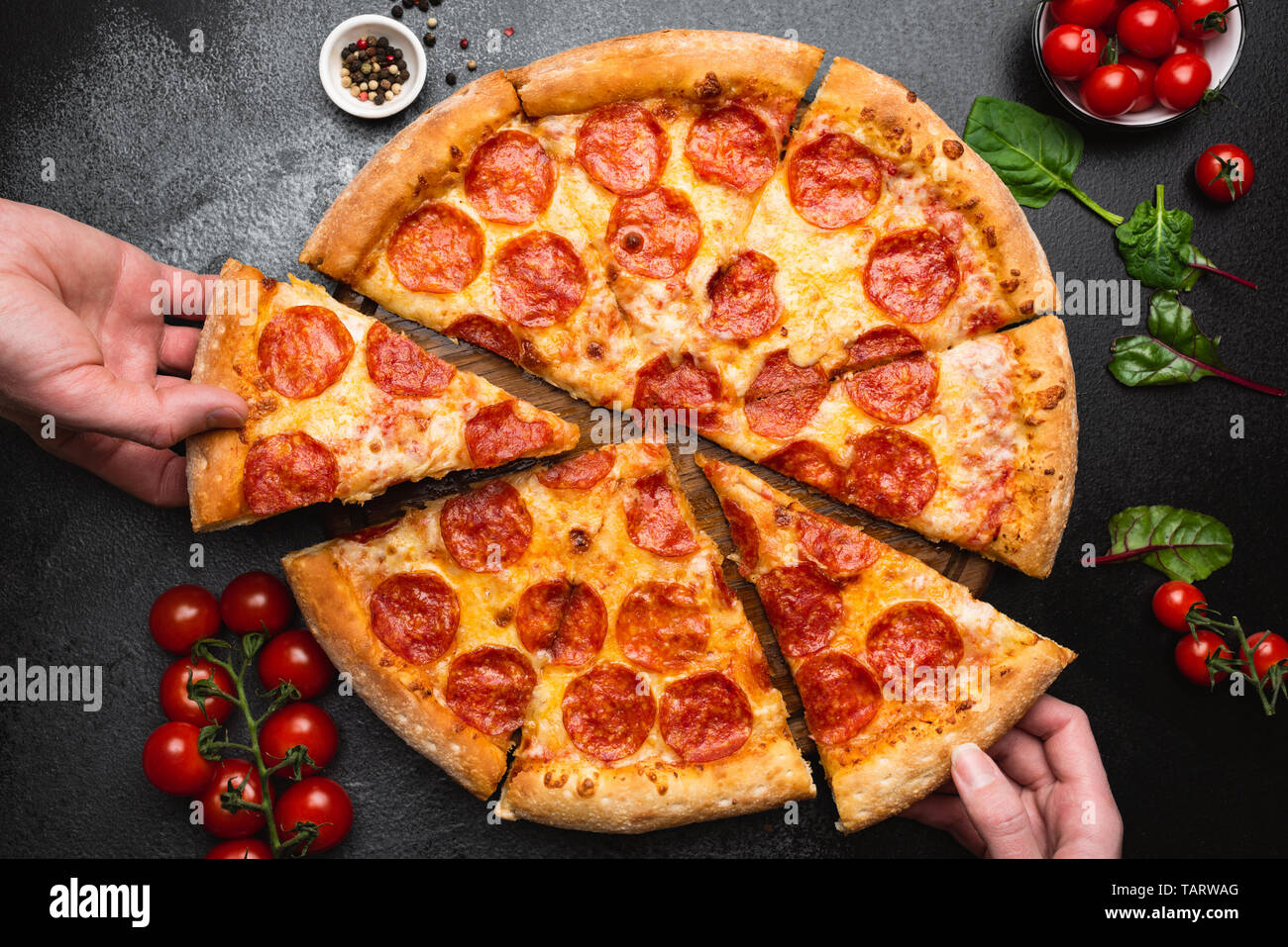Pepperoni pizza on black concrete background top view. People taking slice of pizza. Party food, unhealthy eating concept Stock Photo
