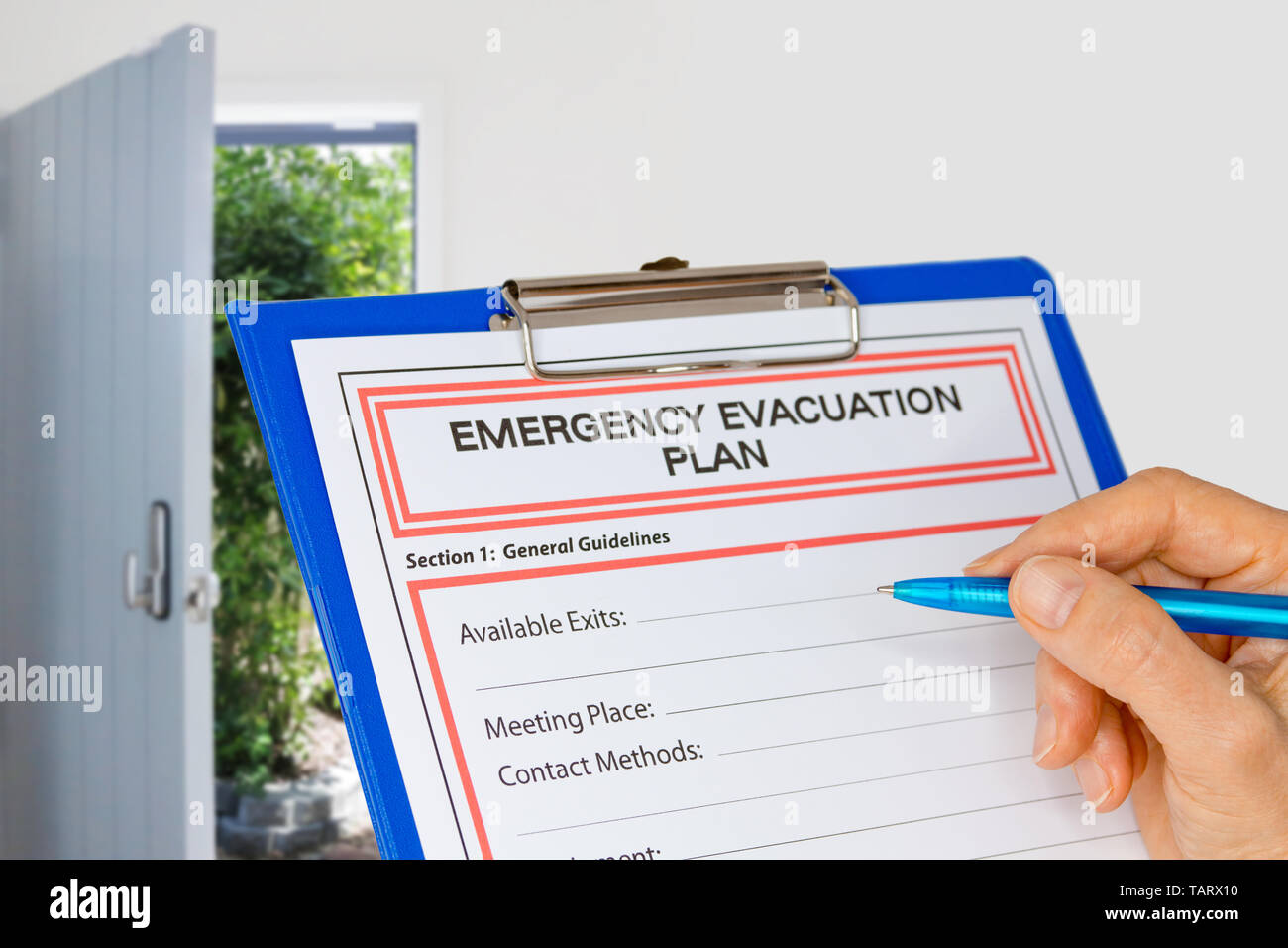 Hand writing an Emergency Evacuation Plan on clipboard beside Exit Door Focus on hand, pen and page Stock Photo