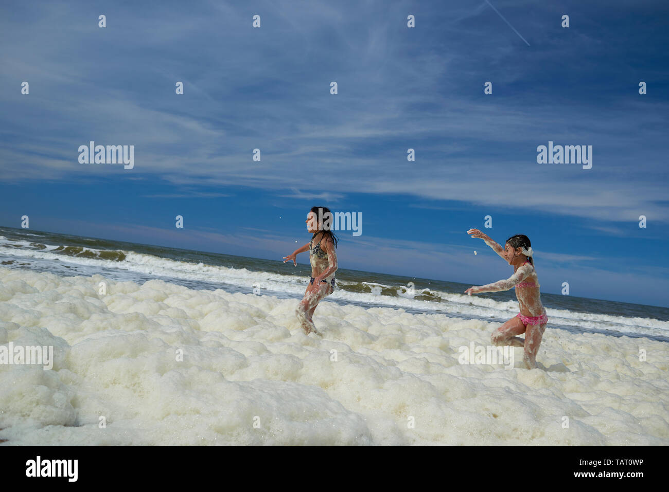 Two little preteen girls having fun running and splashing in sea foam in the ocean at the beach in summer sunshine Stock Photo