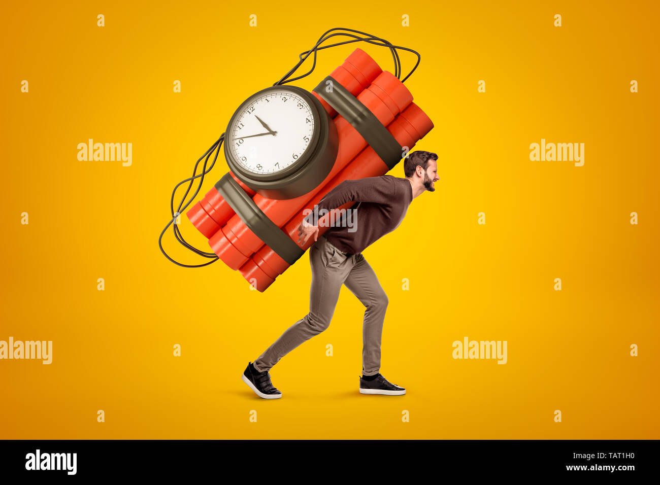 Young man in casual clothes carrying big red dynamite stick time bomb on his back on yellow background Stock Photo