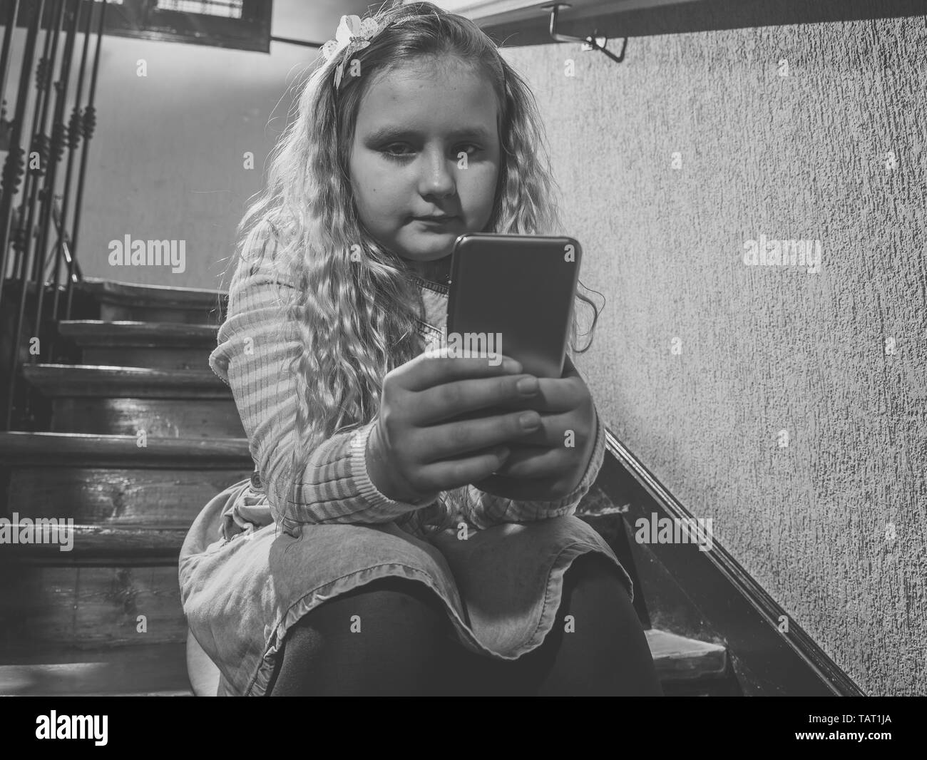 Sad depressed young girl victim of cyberbullying by mobile smart phone sitting on stairs feeling lonely, unhappy, hopeless and abused. Child bullied a Stock Photo