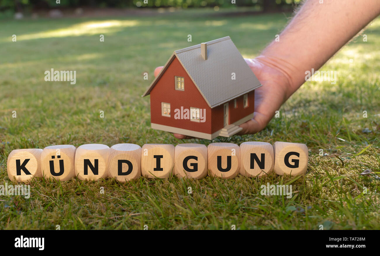 Cubes form the German word "Kuendigung" ("dismissal" in English) in front of a model house. Stock Photo