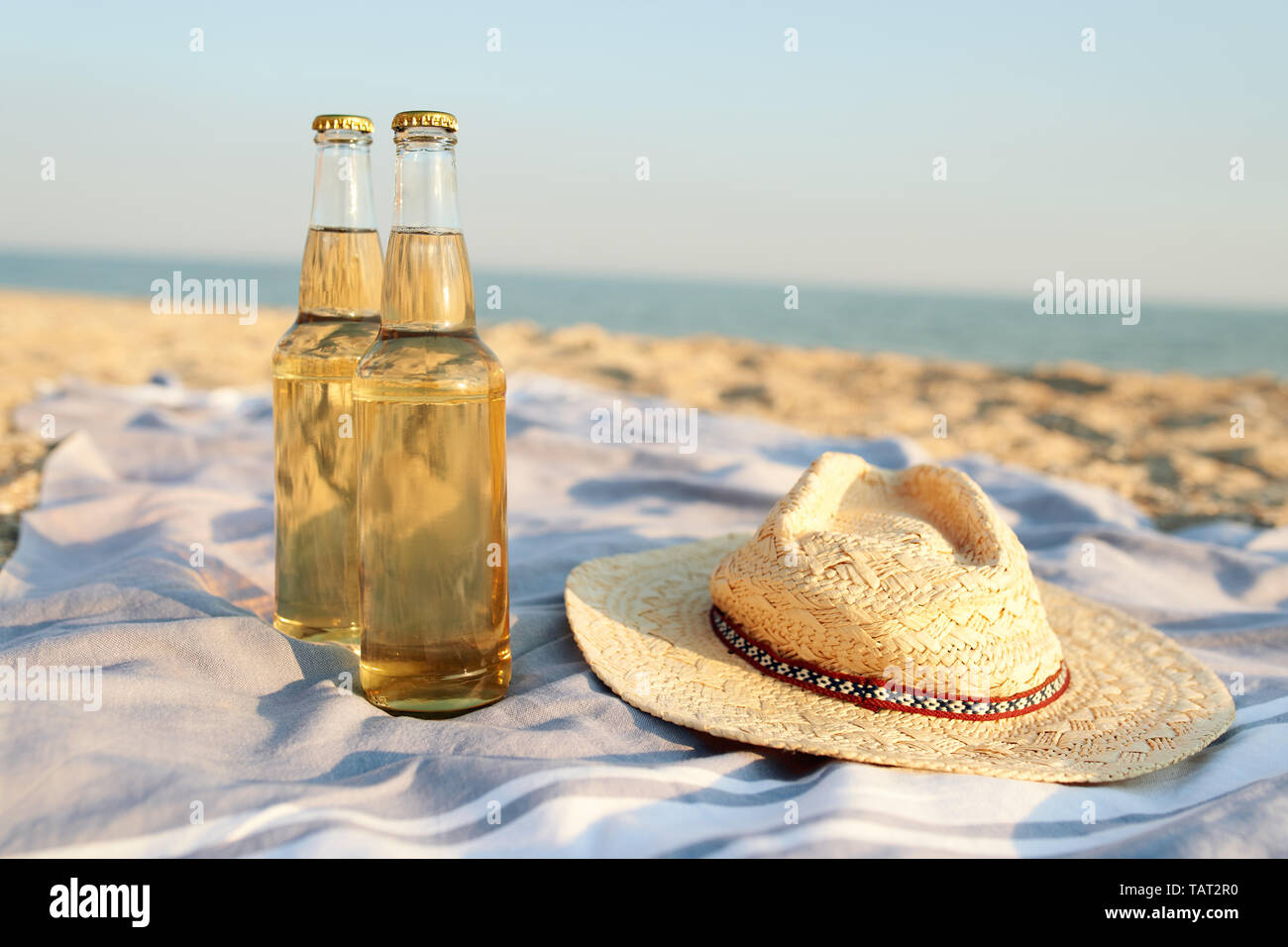 Closeup of two beer glass bottles on sandy tropical beach towel near straw hat. Blue ocean lagoon on background. Refreshing beverage on hot summer day Stock Photo