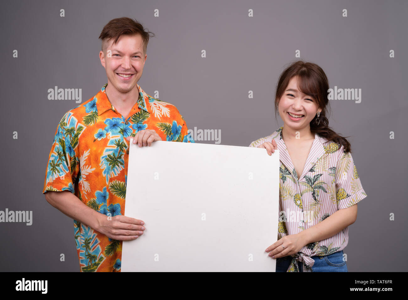 Multi ethnic tourist couple smiling and holding empty white board Stock Photo