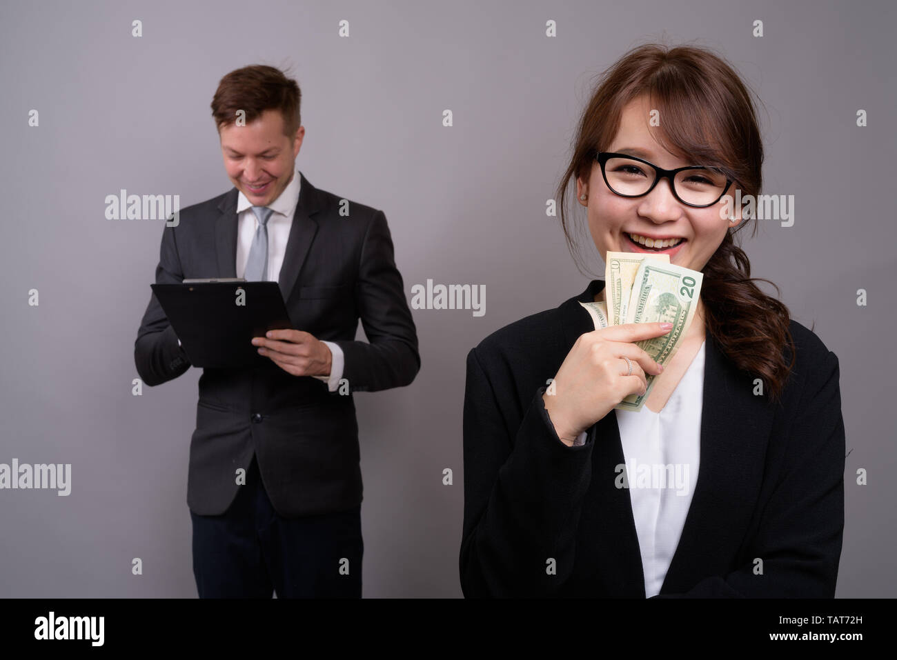Young businessman and young Asian businesswoman against gray bac Stock Photo