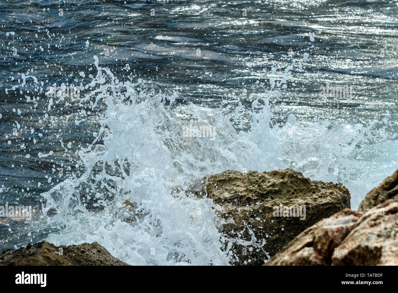 The foam of the surf on coastal rocks. The sea wave breaks from the stone. Stock Photo