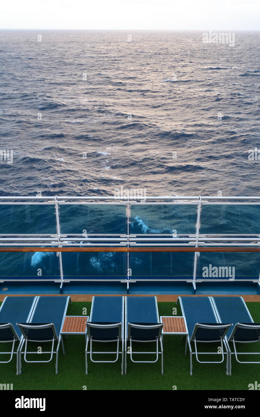 Blue sun loungers on the green deck of the ship overlooking the sea and the waves. Stock Photo