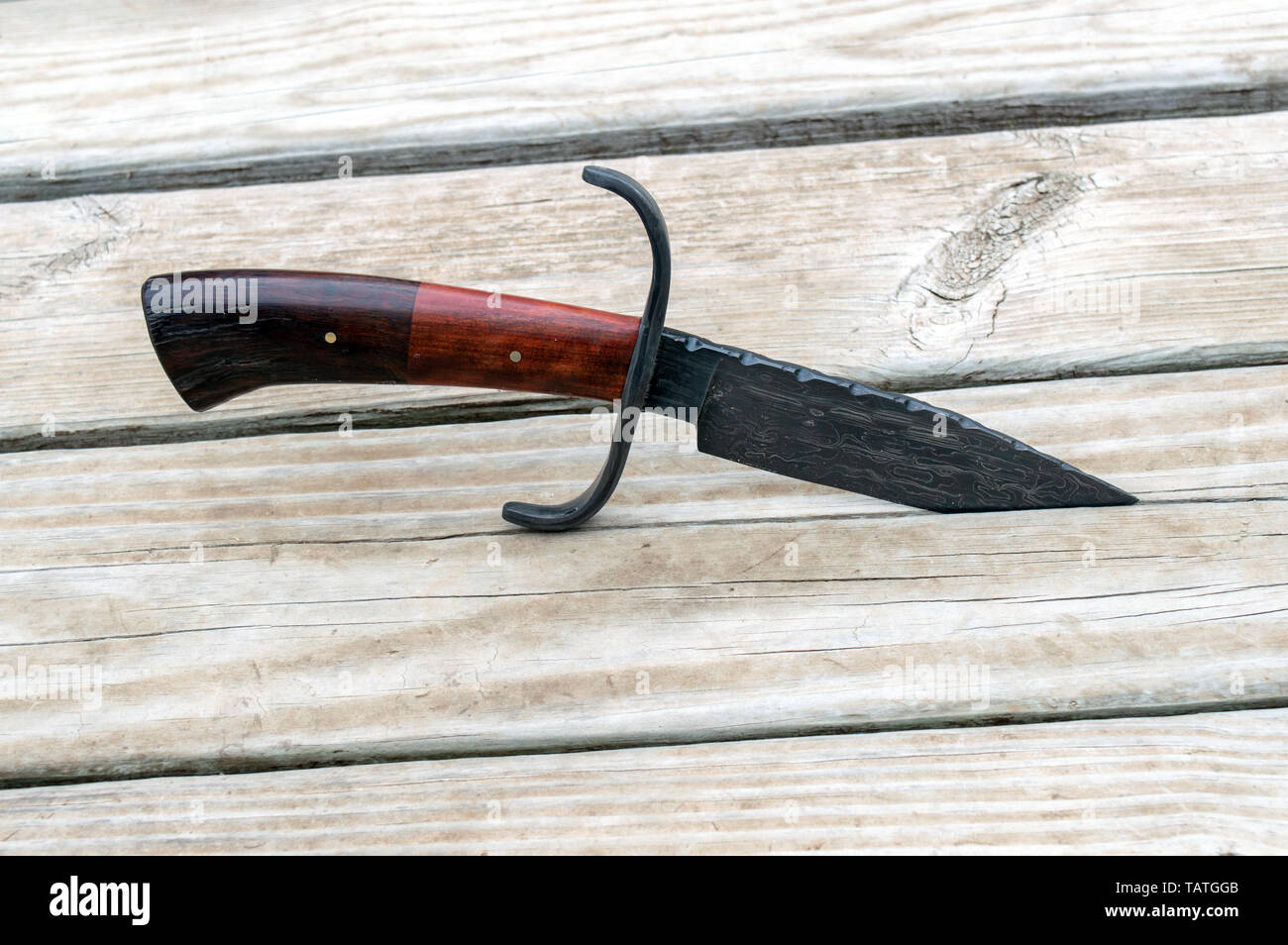 A Damascus bowie knife displayed on the back deck with bokeh effect. The two colored handle is made from Desert Ironwood, also known as Red Heart. Stock Photo