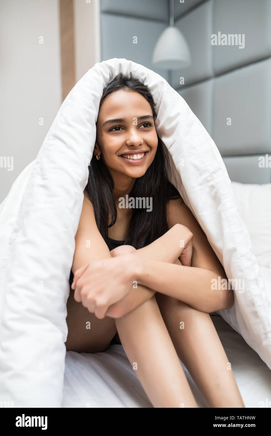 Portrait of a happy young woman lying in bed under the blanket at home and screaming Stock Photo