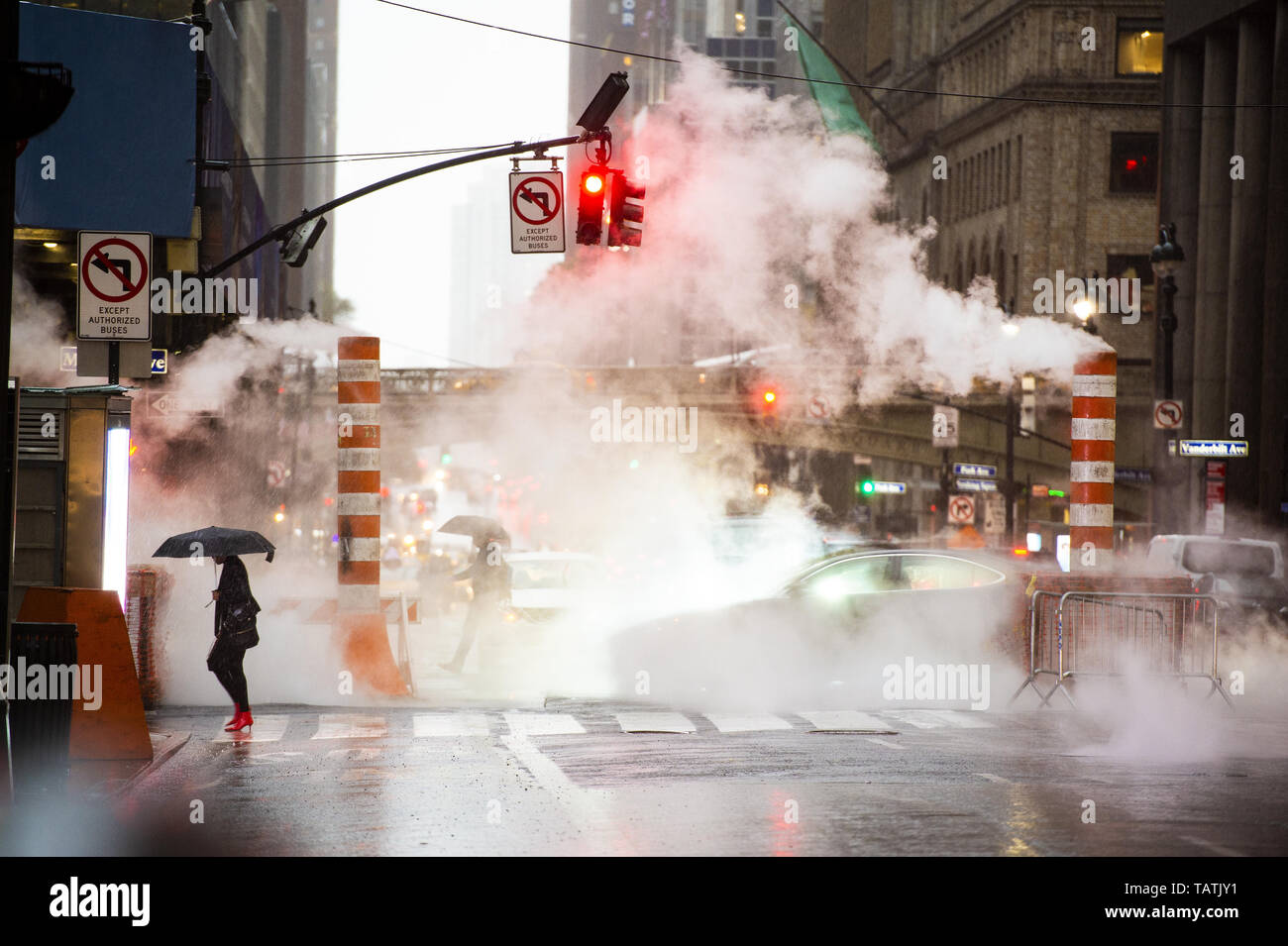 A woman with an umbrella and red high heels shoes is crossing the 42nd street in Manhattan. Cars and steam coming out from from the manholes. Stock Photo
