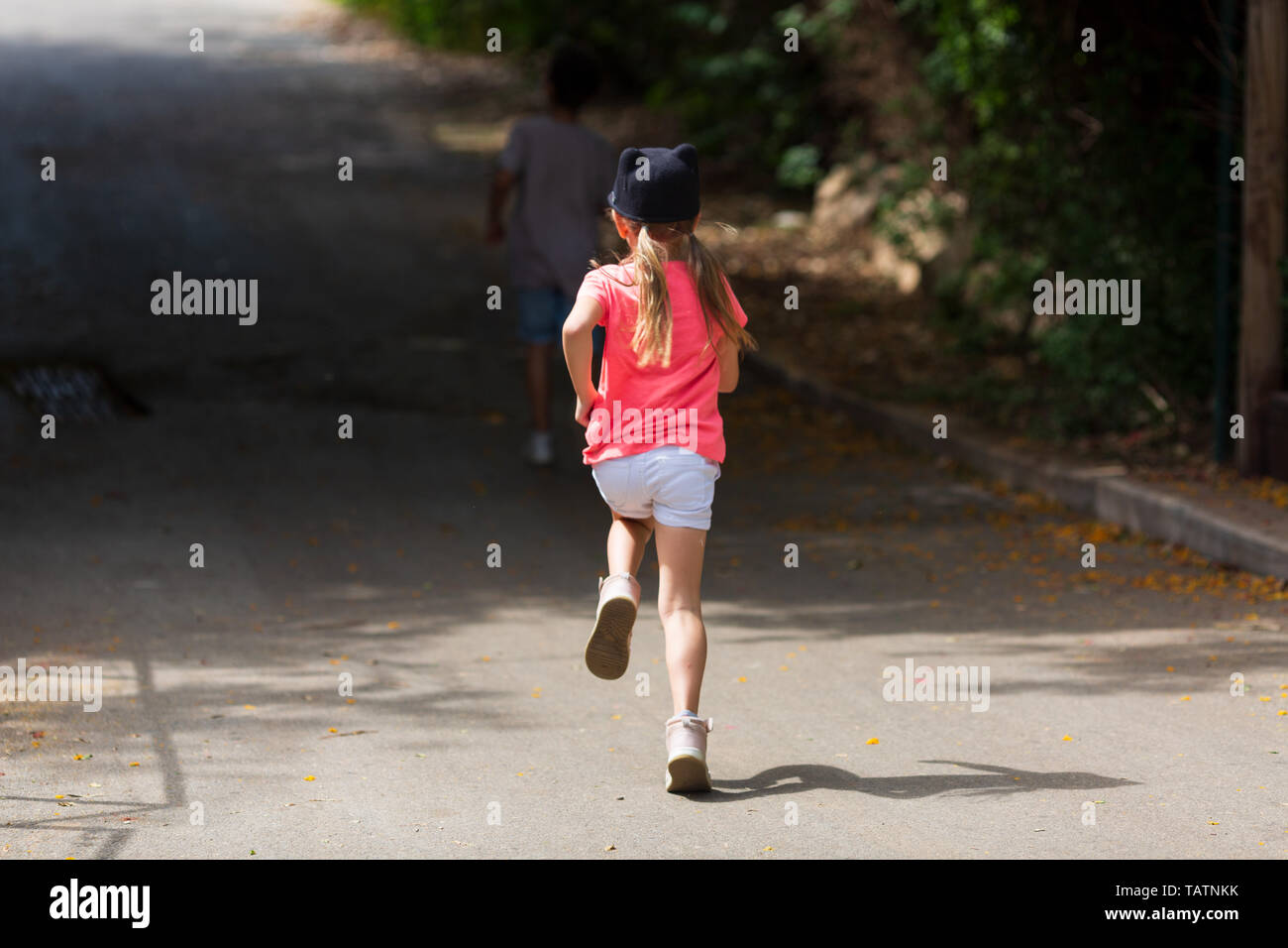 Children run on park walkway into arch made of green plants, rear view ...