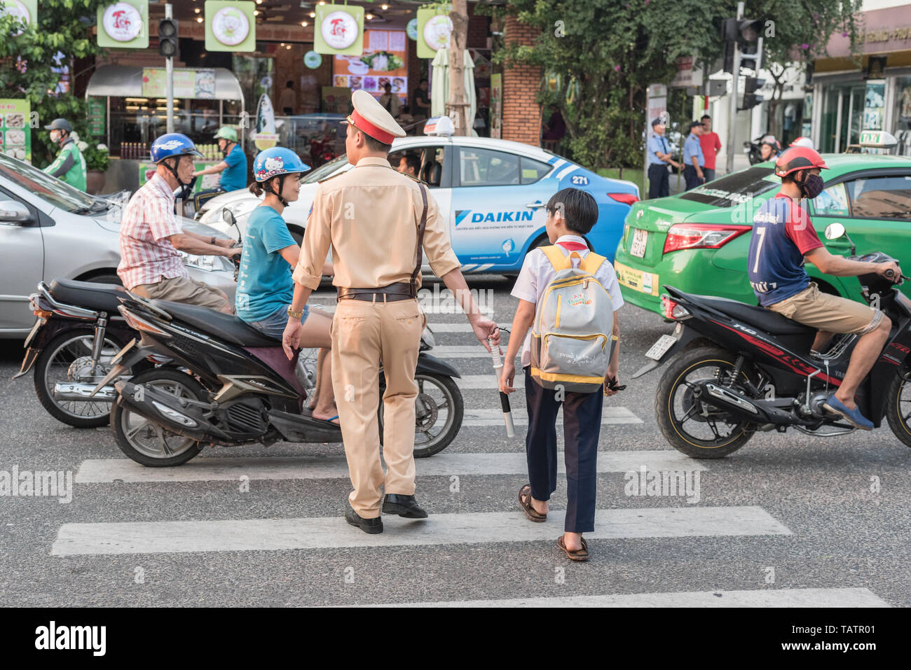 Da Nang, Vietnam - March 21, 2019: a Vietnamese traffic policeman takes a boy across the busy street. Stock Photo