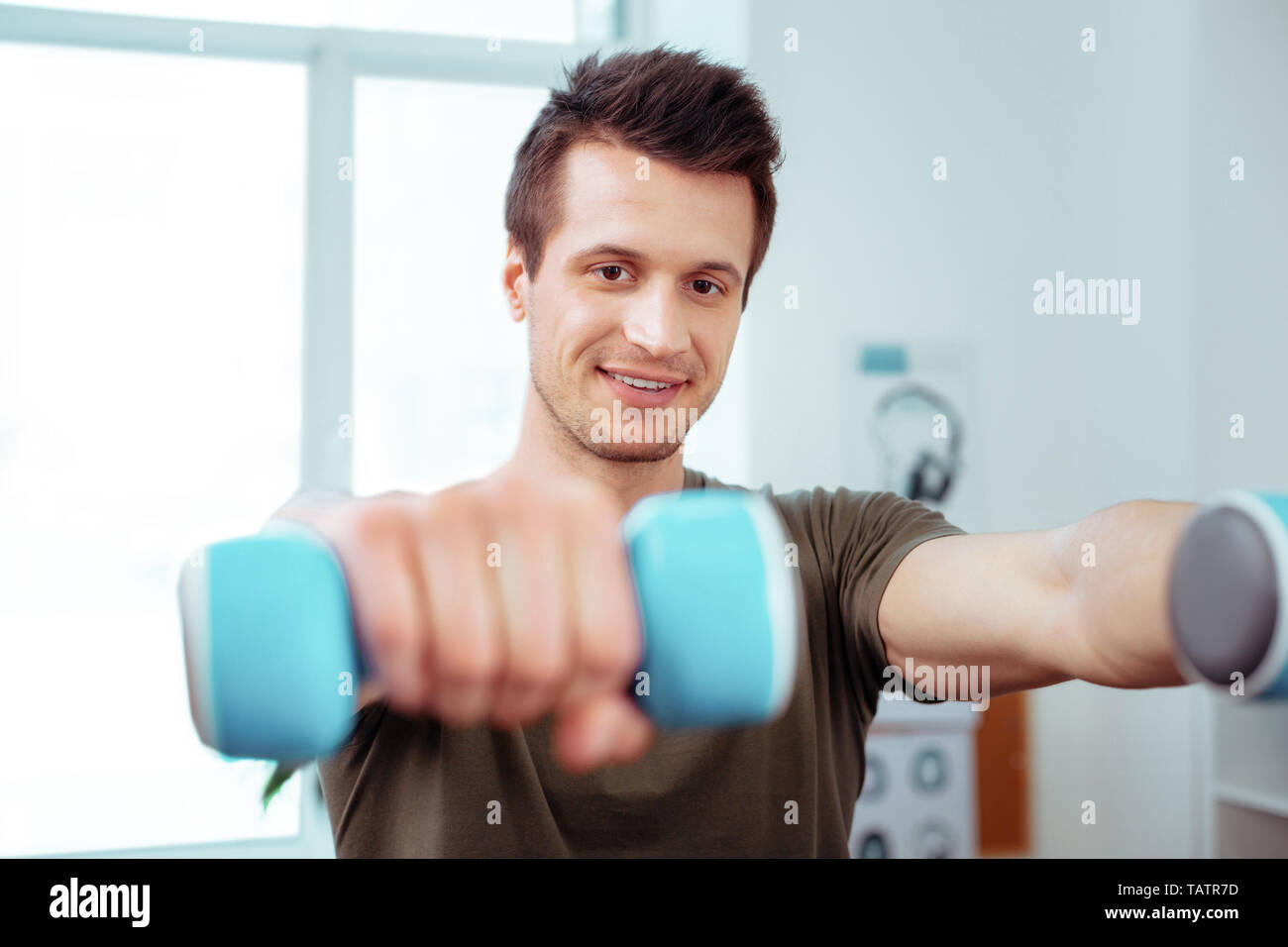 Training with dumbbells. Joyful nice man training with dumbbells while having a morning gymnastics Stock Photo