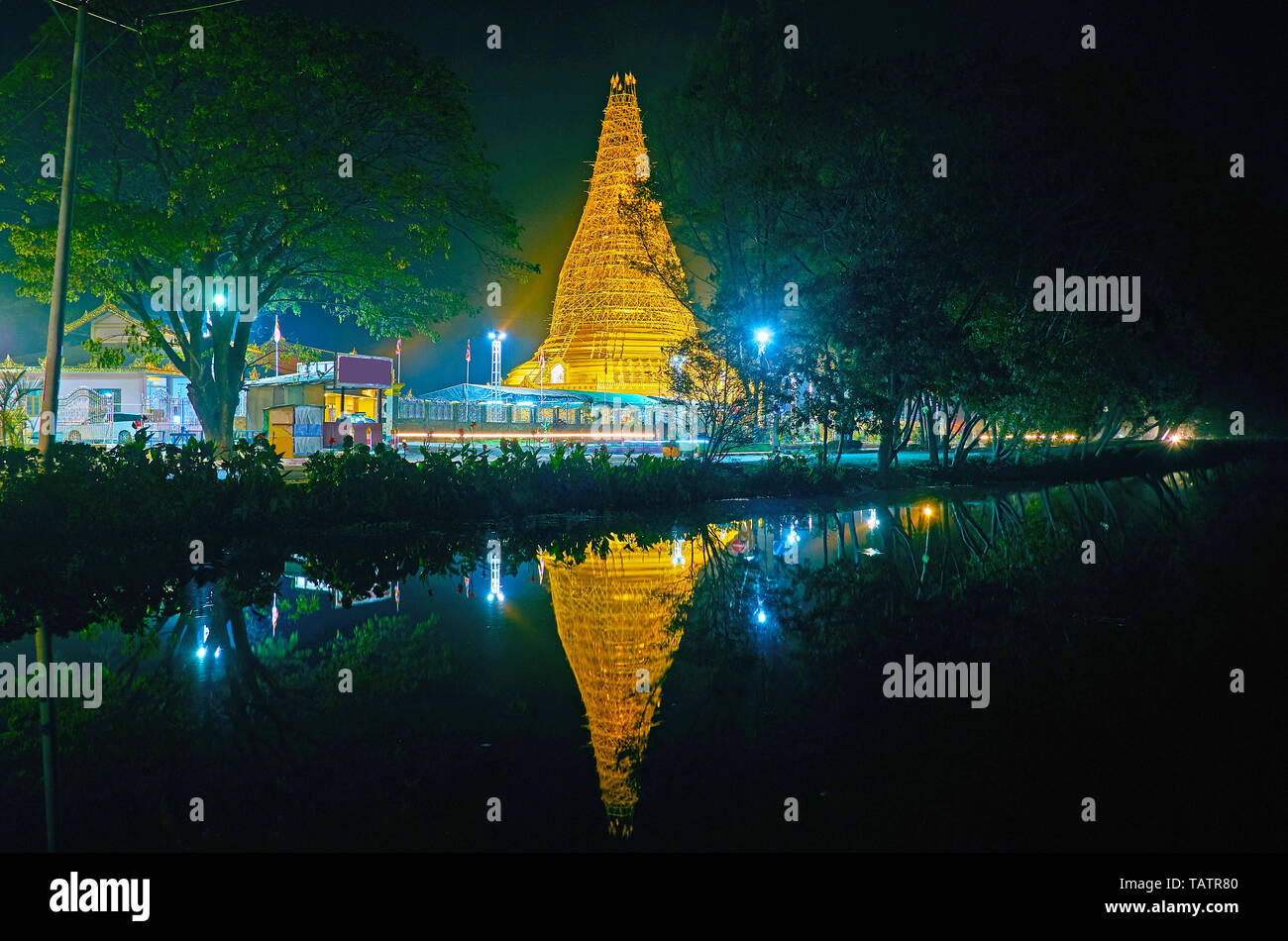 The evening walk along the Tharzi Pond with a view on large golden supa of local Buddhist temple and its reflection in dark water, Nyaungshwe, Myanmar Stock Photo